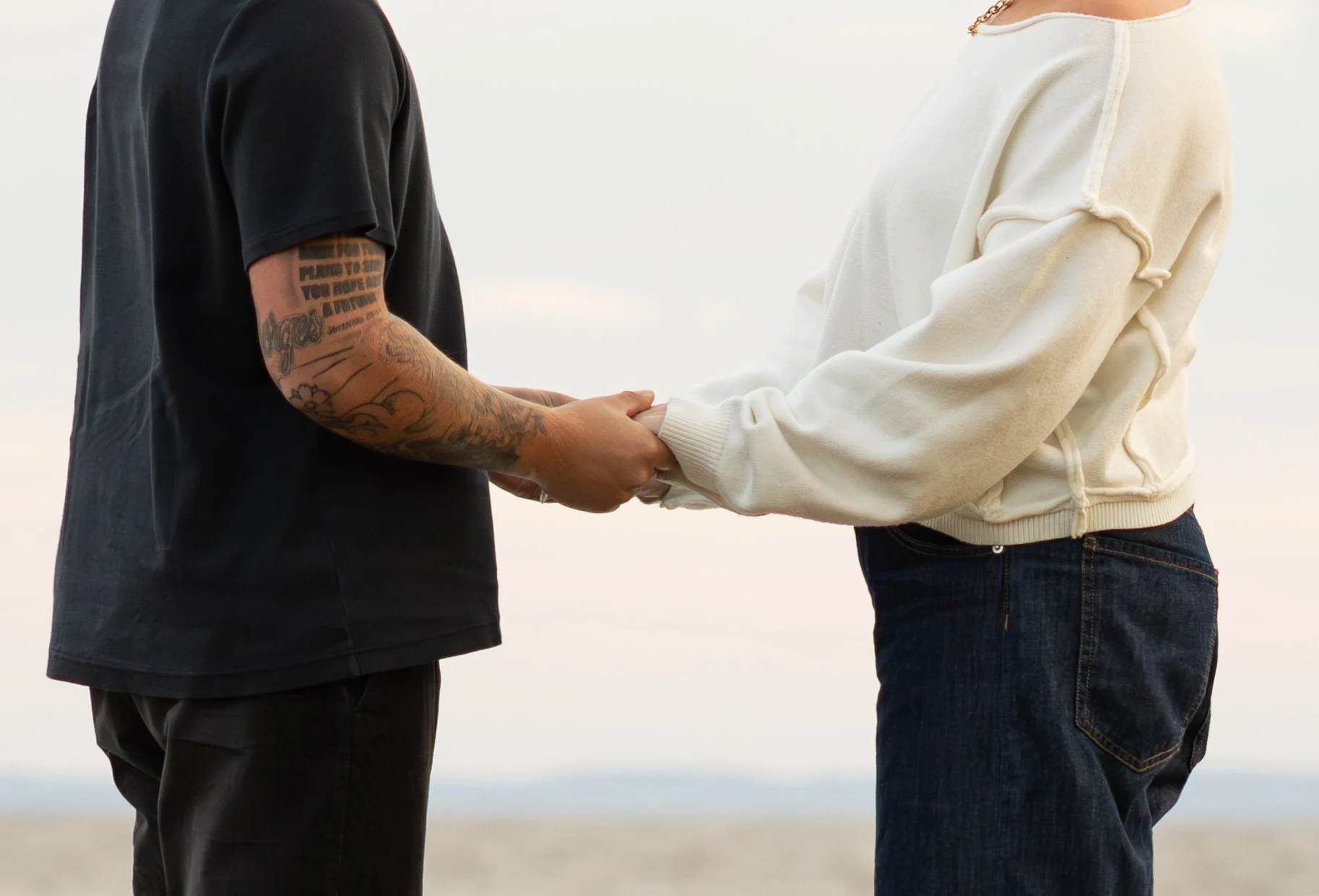 Couple holding hands outdoors, focus on their hands and upper bodies, with the sky in the background.
