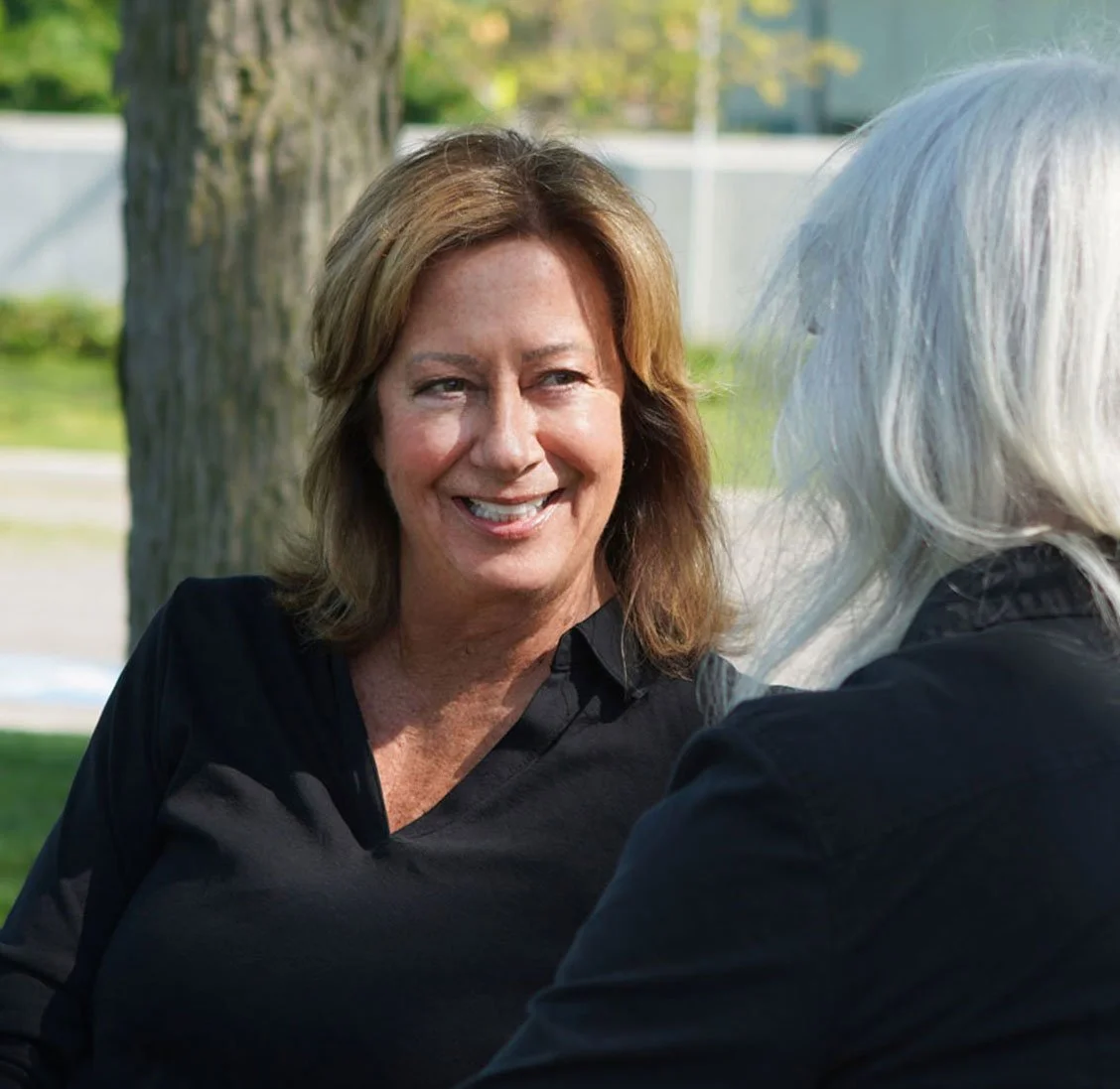 Two women sitting on a park bench having a conversation on a sunny day.