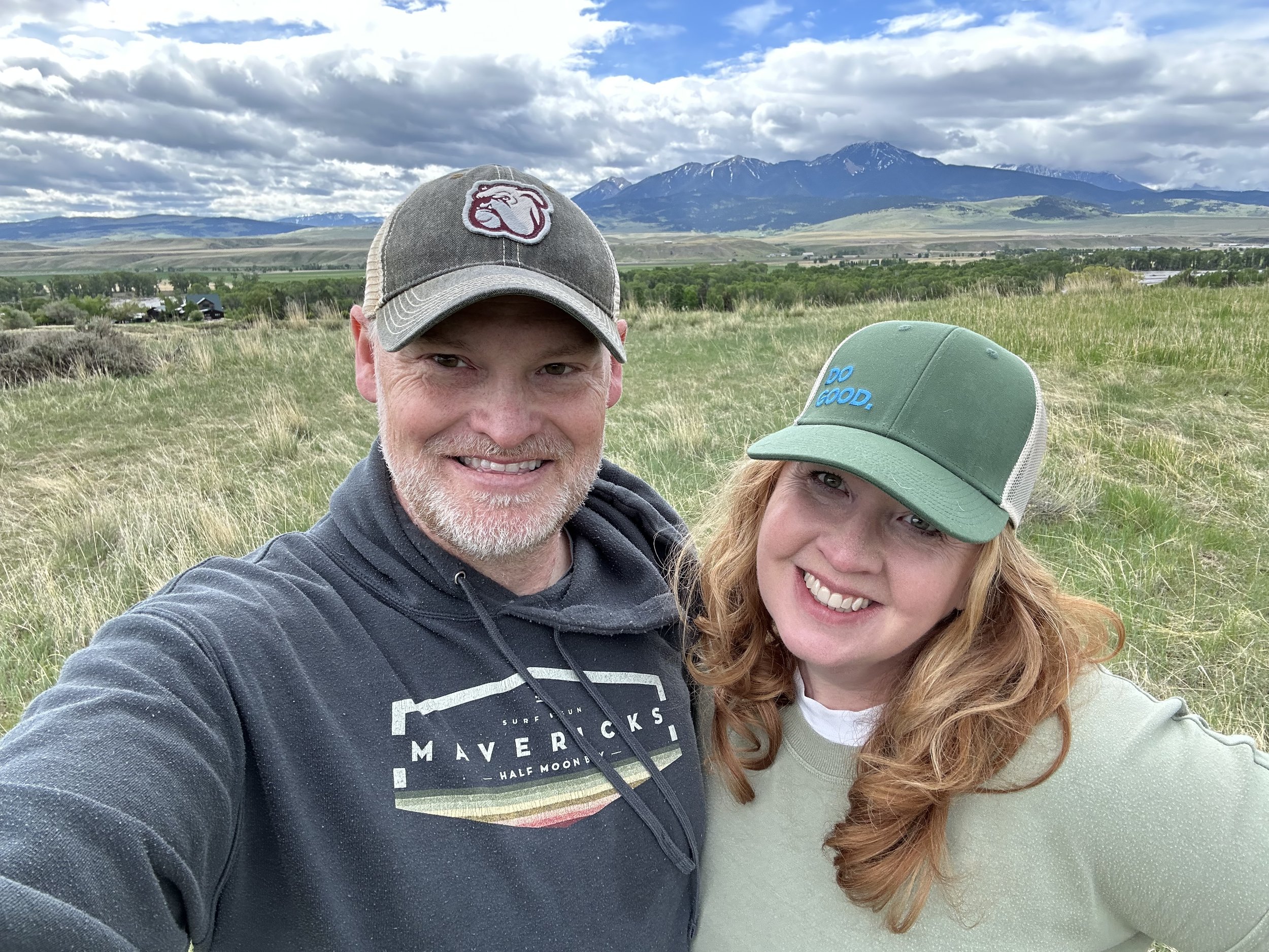 Man and woman selfie in a Montana meadow with mountains in the background