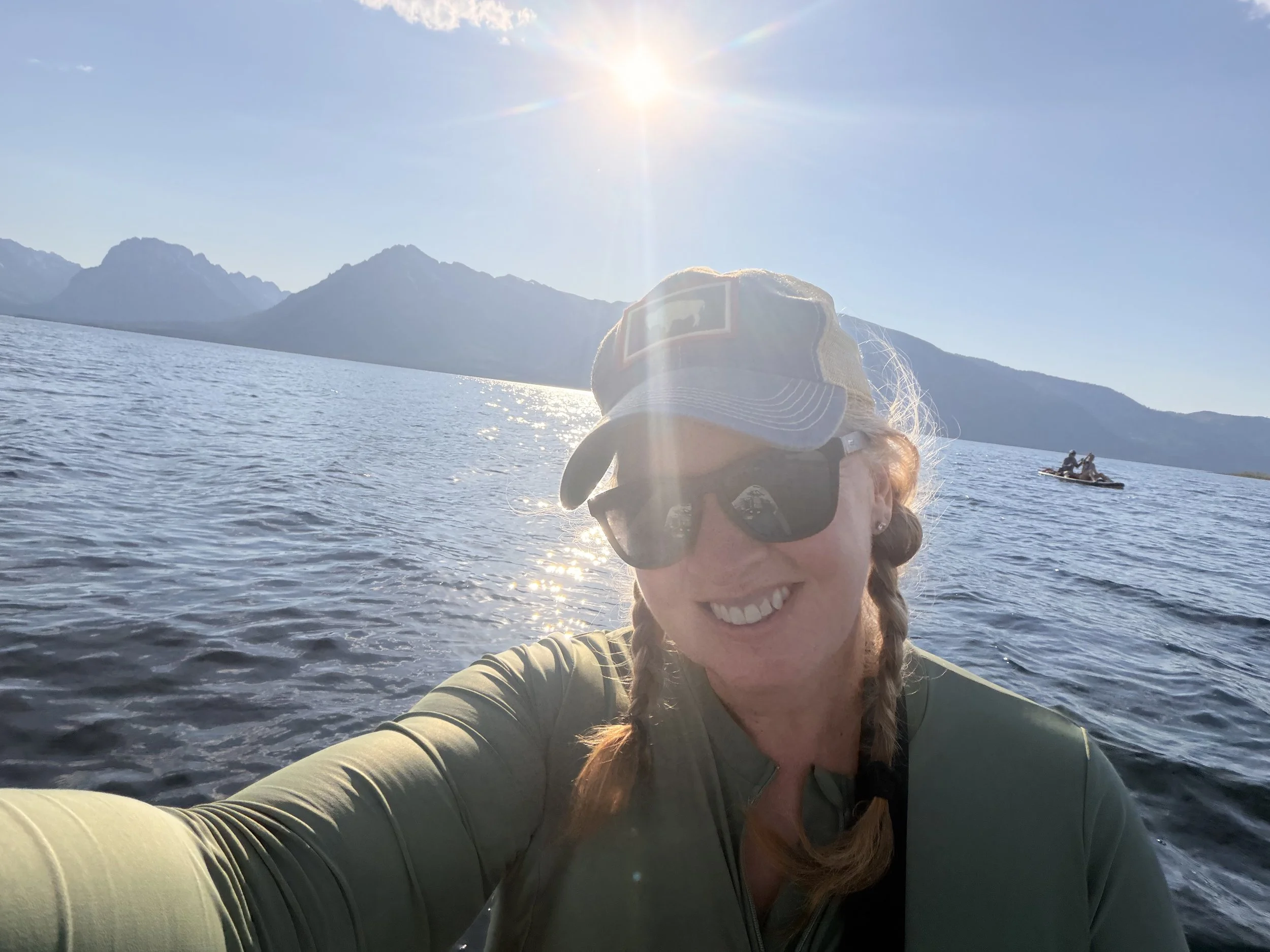 A woman sitting on a paddleboard on Jackson Lake with the Teton Mountains behind her