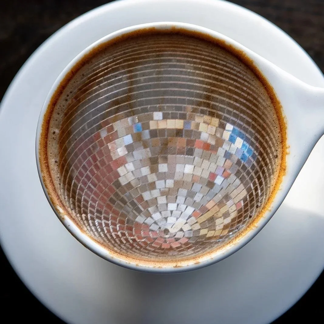 Top view of a cup of black coffee on a white saucer, with a mosaic pattern reflected on the surface of the coffee.