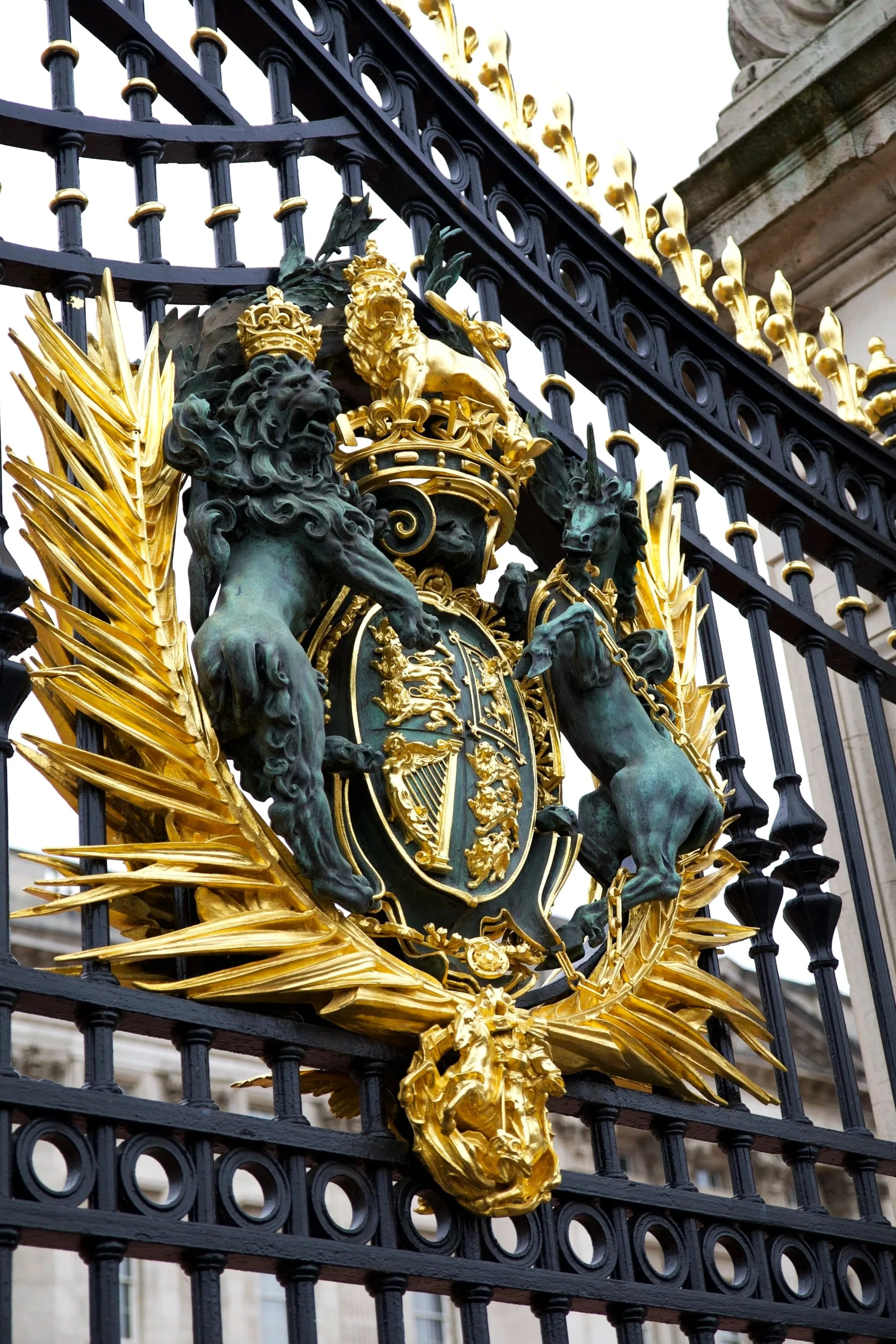 Close-up of a gold and black ornate crest or emblem on a black wrought iron fence, featuring a lion, a unicorn, and crown details.