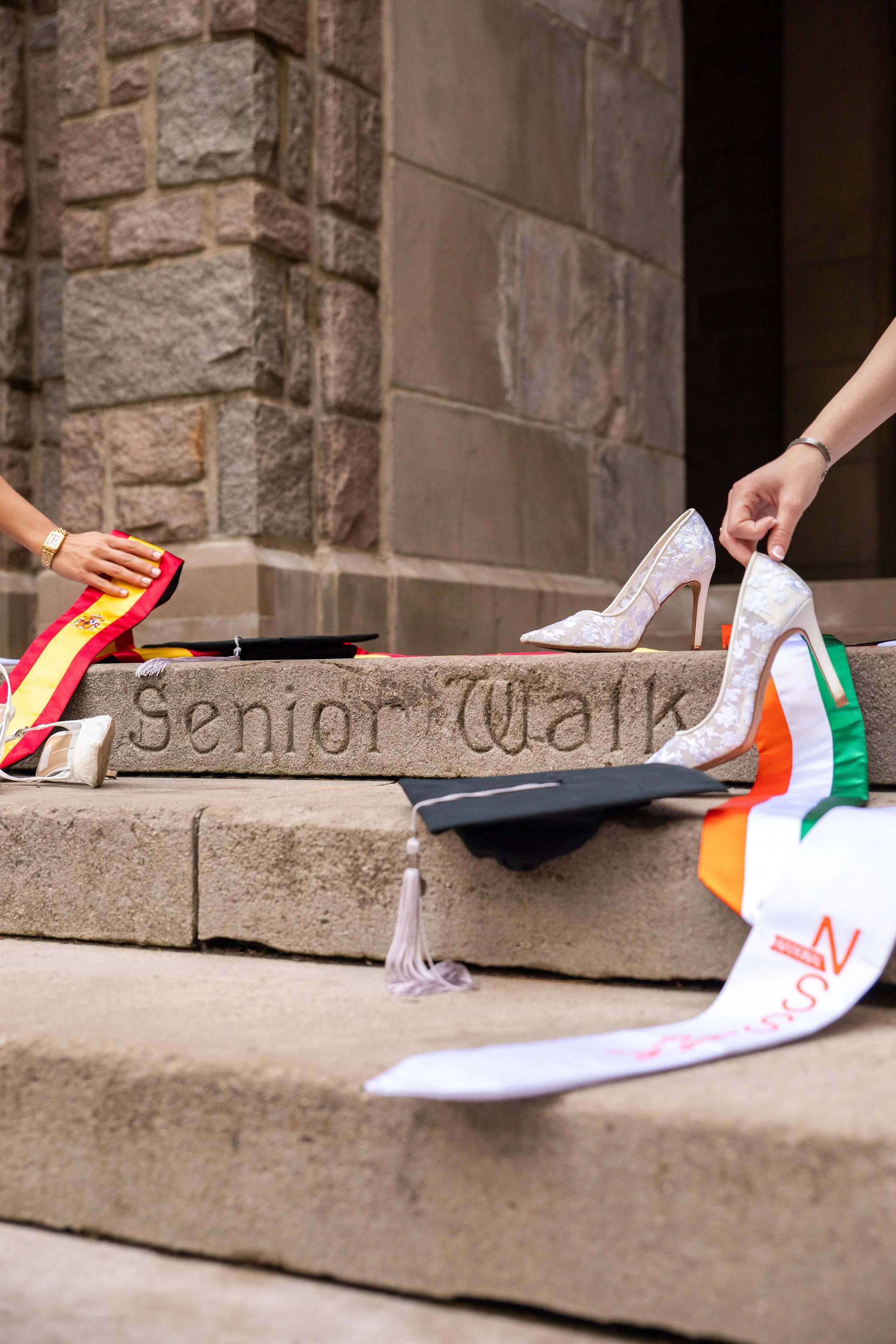 Shoe display on stone steps with a woman holding a white high heel shoe. A sash with the Irish flag colors and other accessories are also visible.