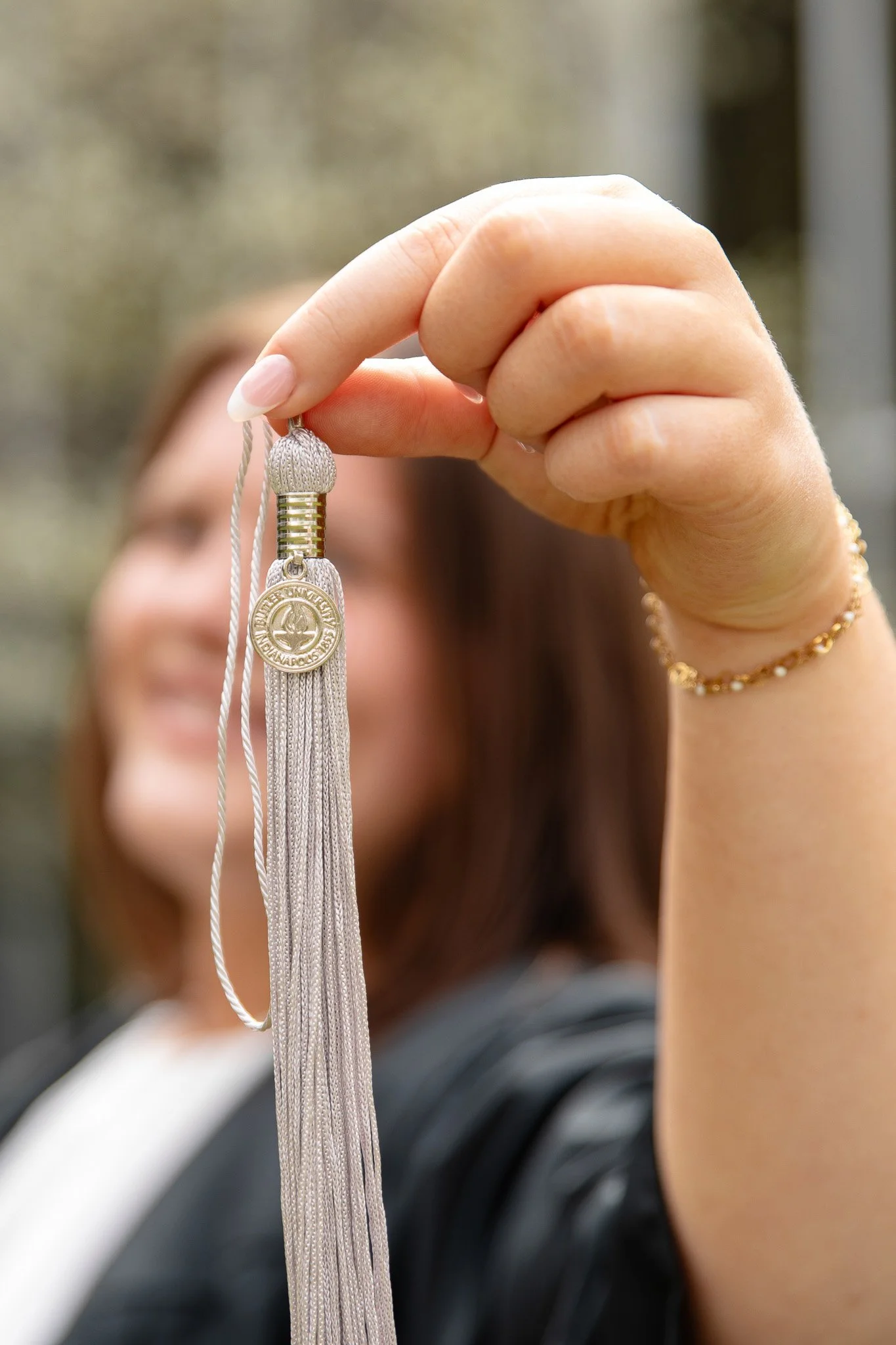 A woman with brown hair holding a medal and tassel, with further people holding similar medals in the background.