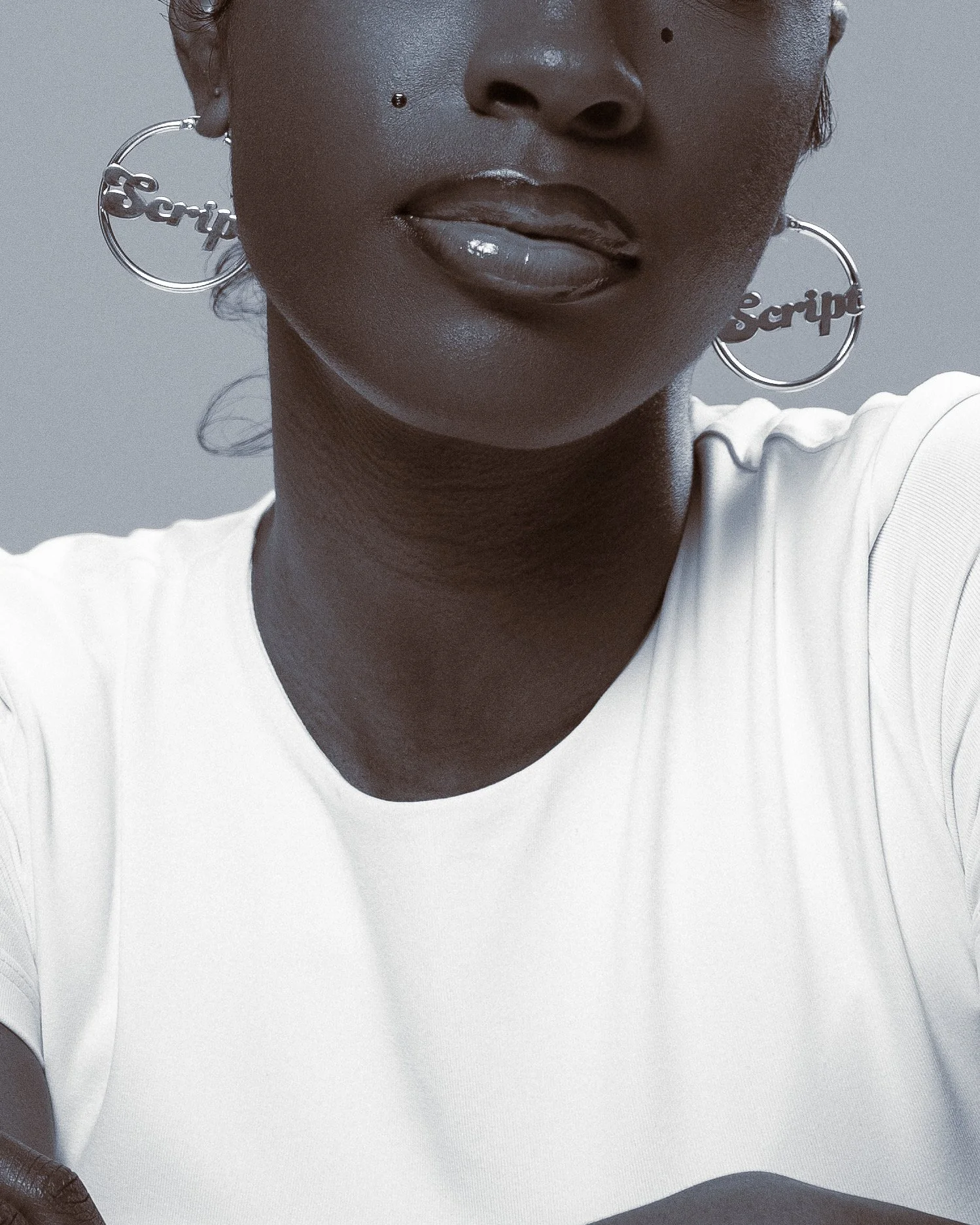 Close-up of a person’s face, showing lips, nose, and earrings with the word "Barbie" in hoop earrings. The person is wearing a white shirt.