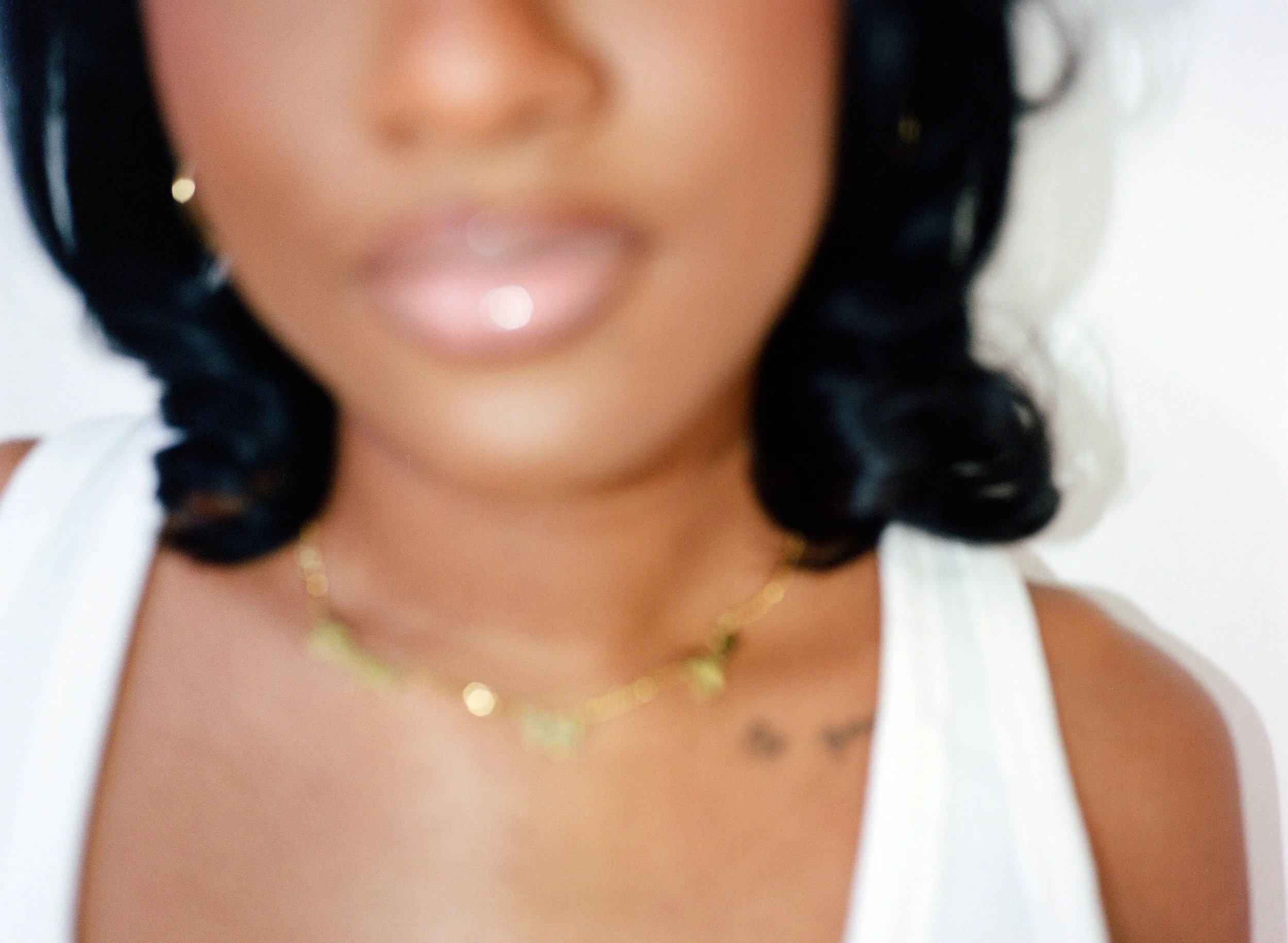 Close-up of a woman with dark, curly hair wearing gold jewelry, including earrings and necklaces, with a blurred background.