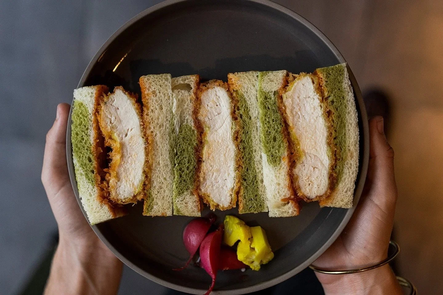 Plate of four chicken katsu sandwiches with pickled vegetables at the bottom