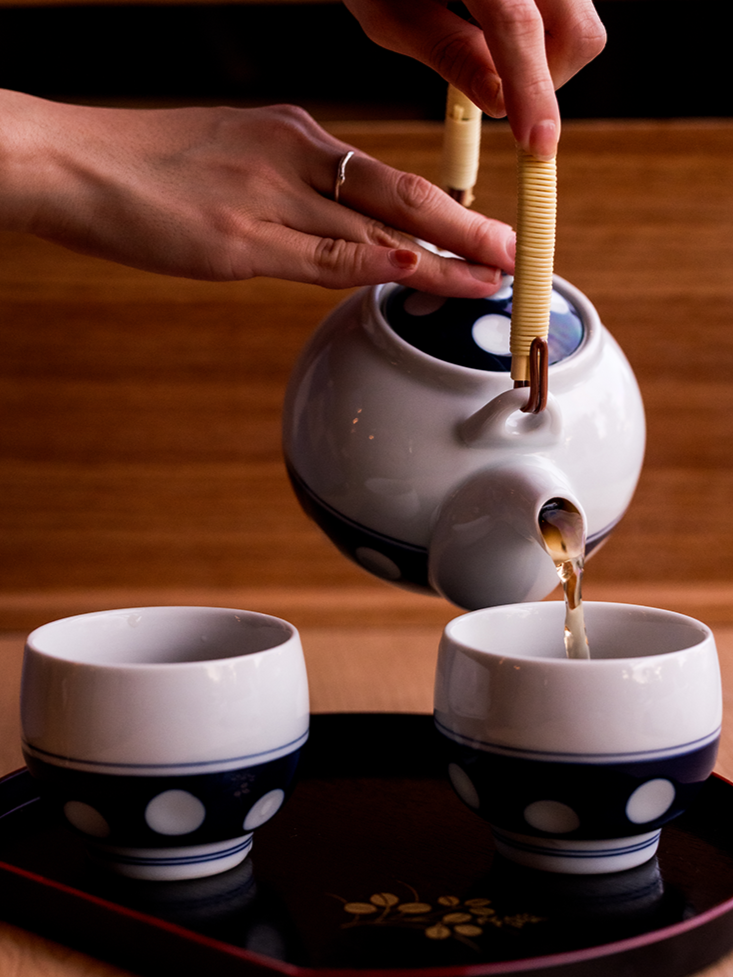 A teapot pouring tea into two matching teacups on a tray.