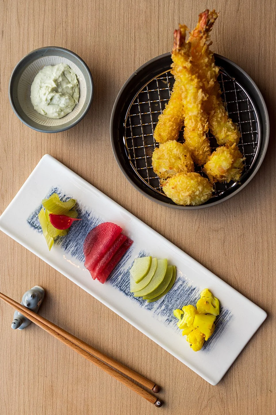 Plate of assorted sashimi with slices of tuna, yellowtail, and other fish, pickled vegetables, wasabi, and dipping sauce, alongside tempura shrimp and vegetables with a side of wasabi and dipping sauce.