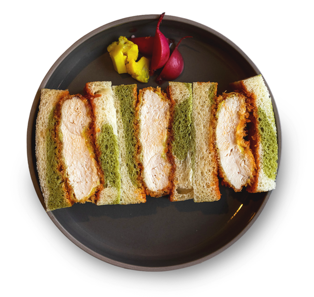Plate with four fried chicken sandwiches with white buns and green lettuce, accompanied by three small sliced radishes and pickled ginger.