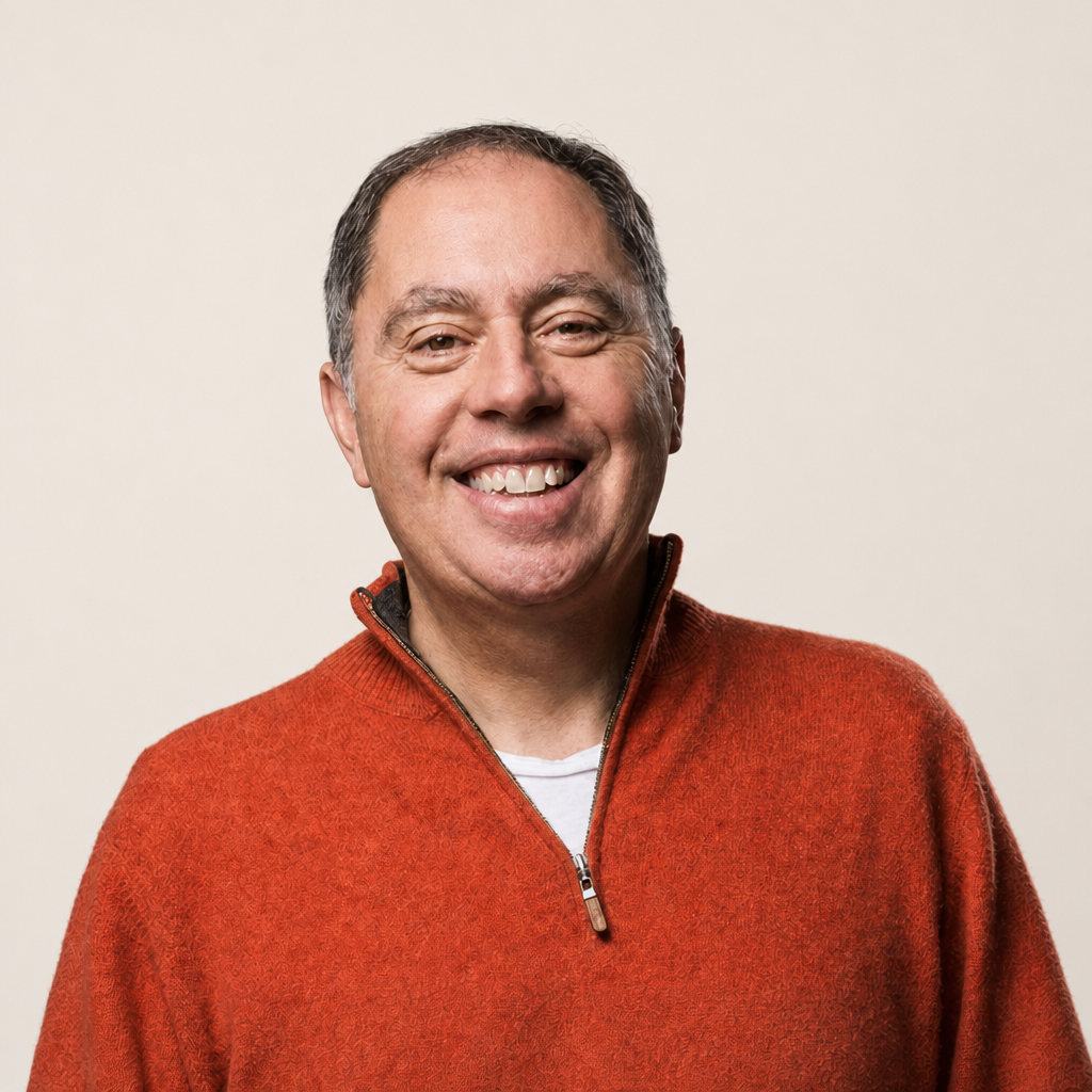 Smiling middle-aged man with short hair wearing a red zip-up sweater over a white shirt, standing against a plain light background.
