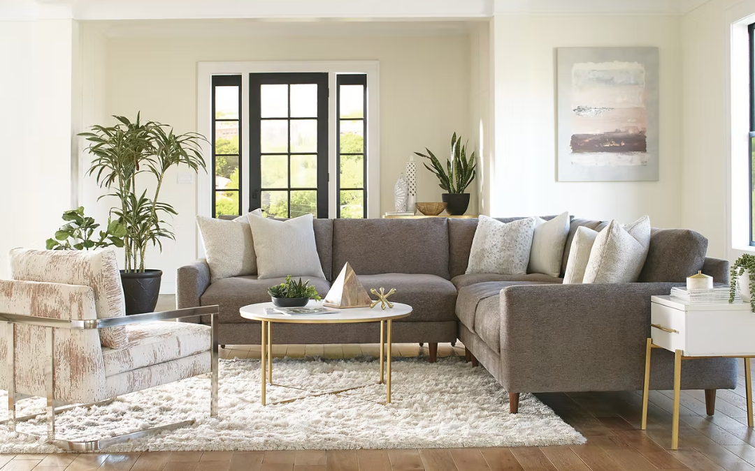 Sala de estar con sofá gris, sillón con tapizado en tonos claros, mesa de centro redonda con decoración, alfombra blanca, plantas y cuadro en la pared