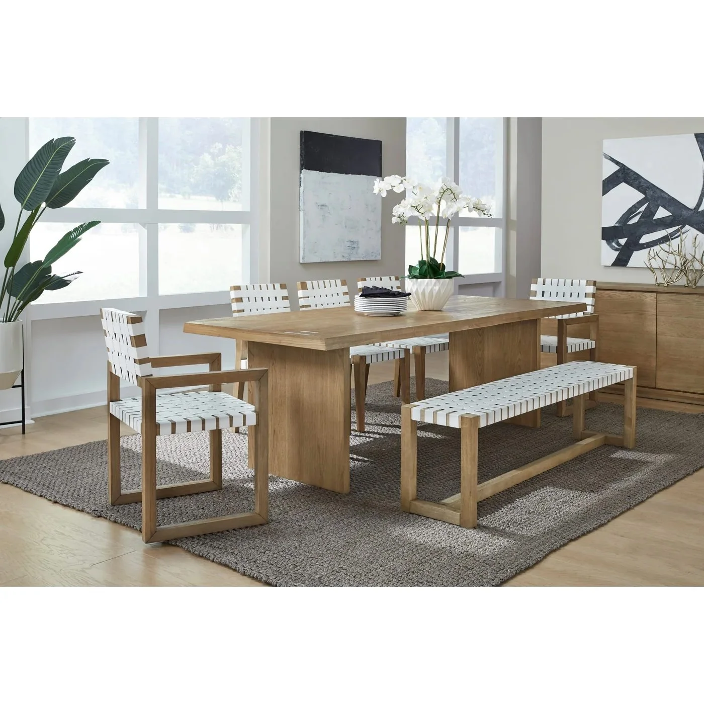 Comedor moderno con mesa de madera y sillas con cojines blancos y rayas, planta grande y obras de arte en las paredes.