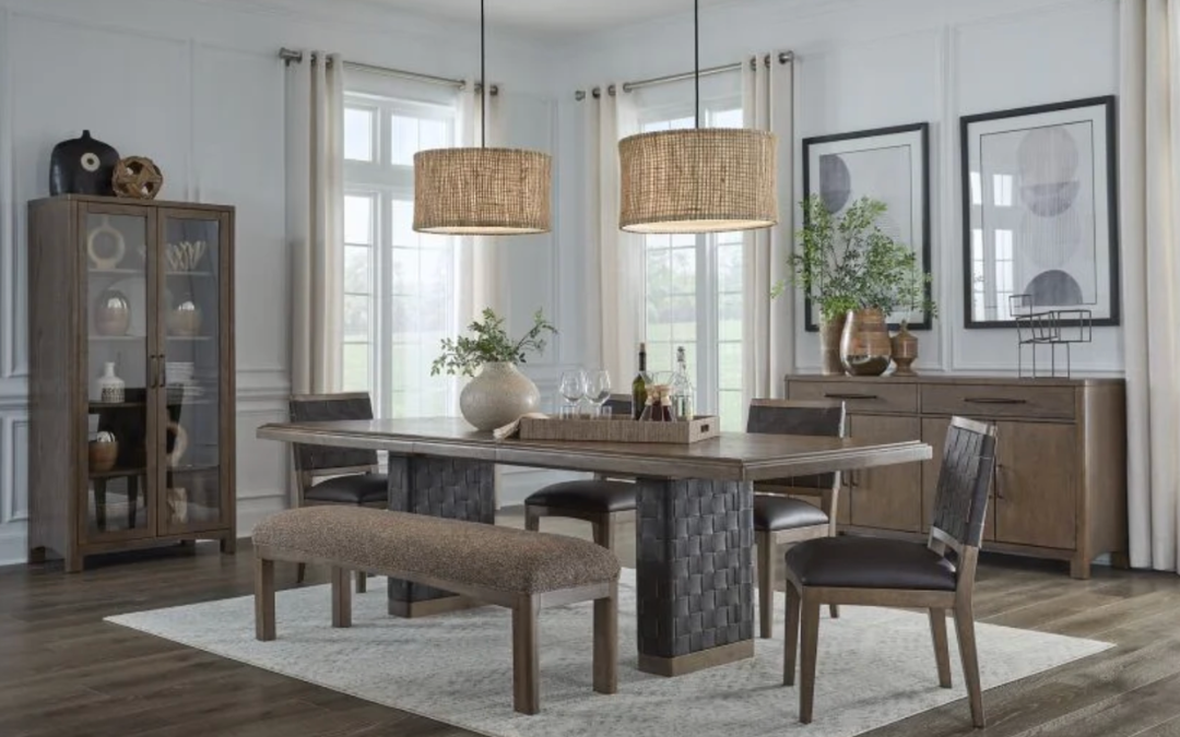 Sala de comedor con mesa de madera, sillas y banco, decorada con cuadros, plantas y objetos decorativos, con ventanas grandes y cortinas blancas.
