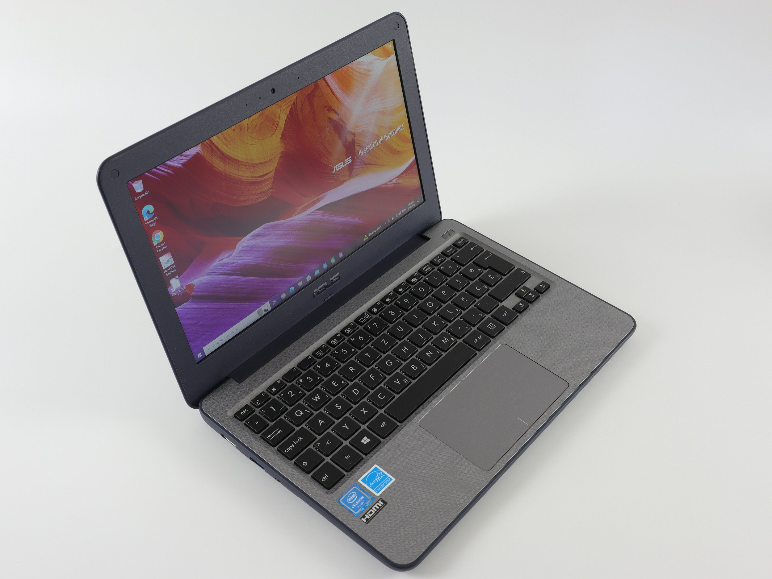 Silver laptop with a colorful display on a white surface, showing the desktop icons and taskbar.