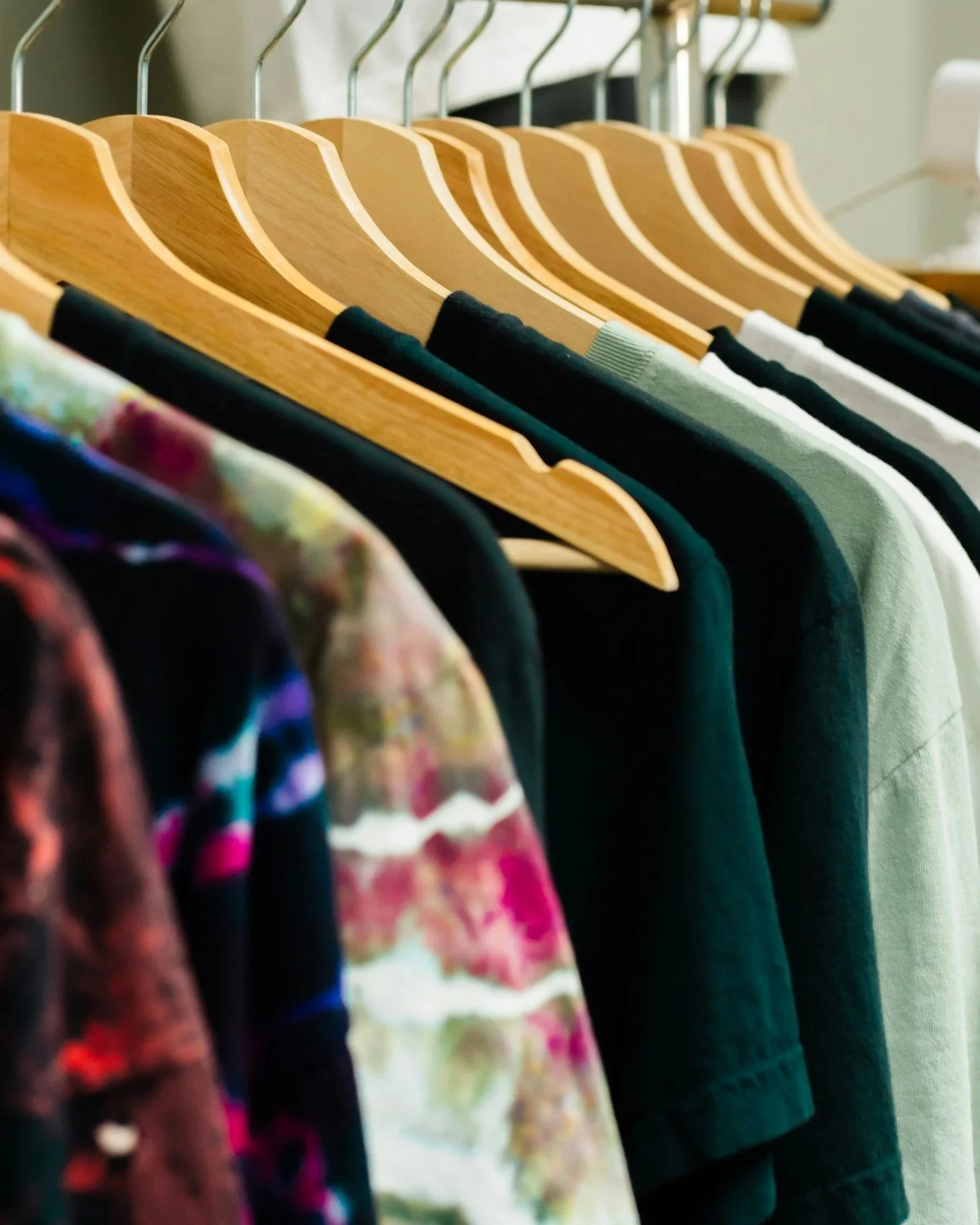 A row of colorful shirts hanging on wooden hangers on a clothing rack.