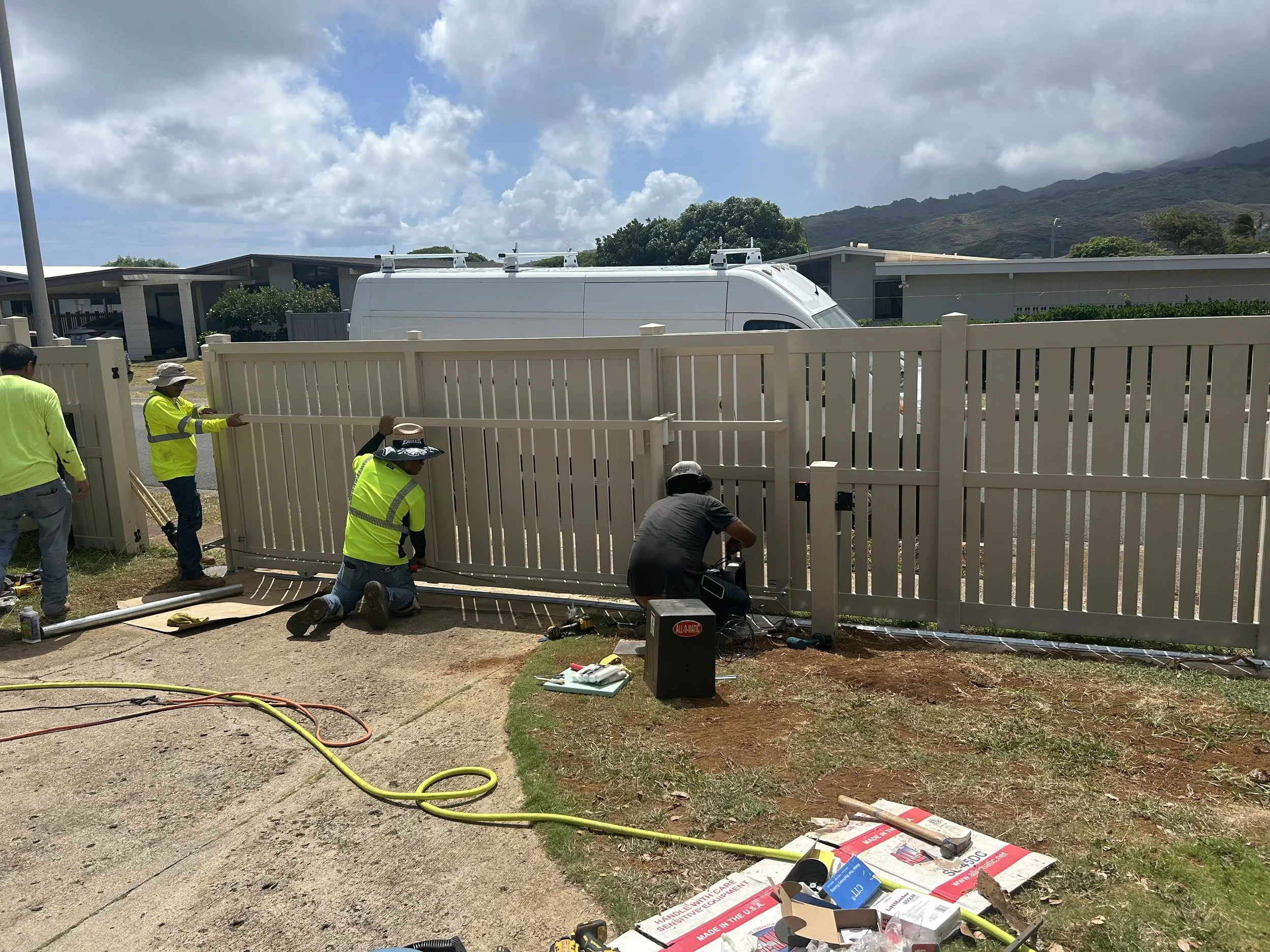 Construction workers installing a white fence in a backyard under partly cloudy sky with mountains in the distance.