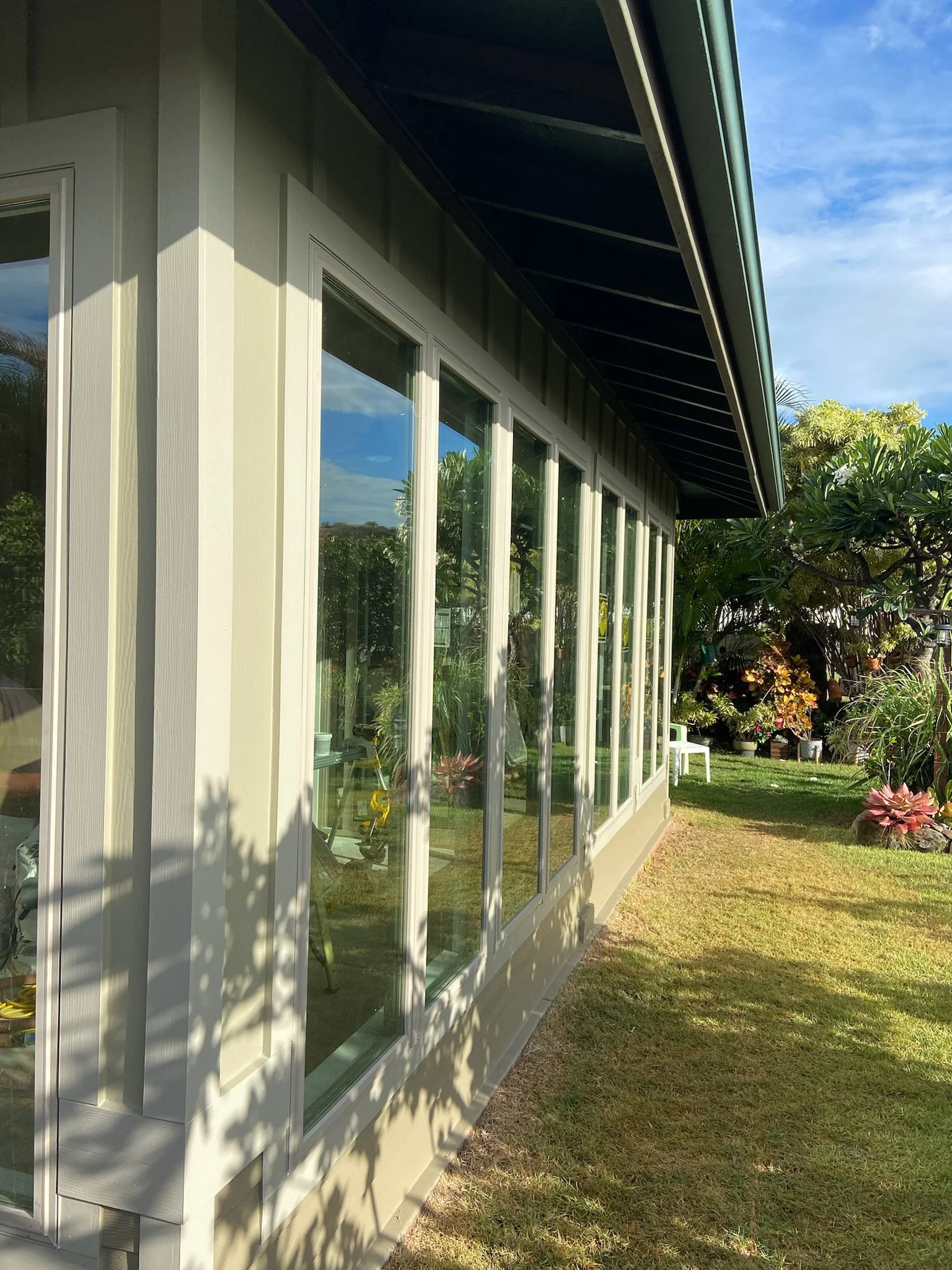 Side view of a house with a large glass enclosure and a garden with plants and flowers