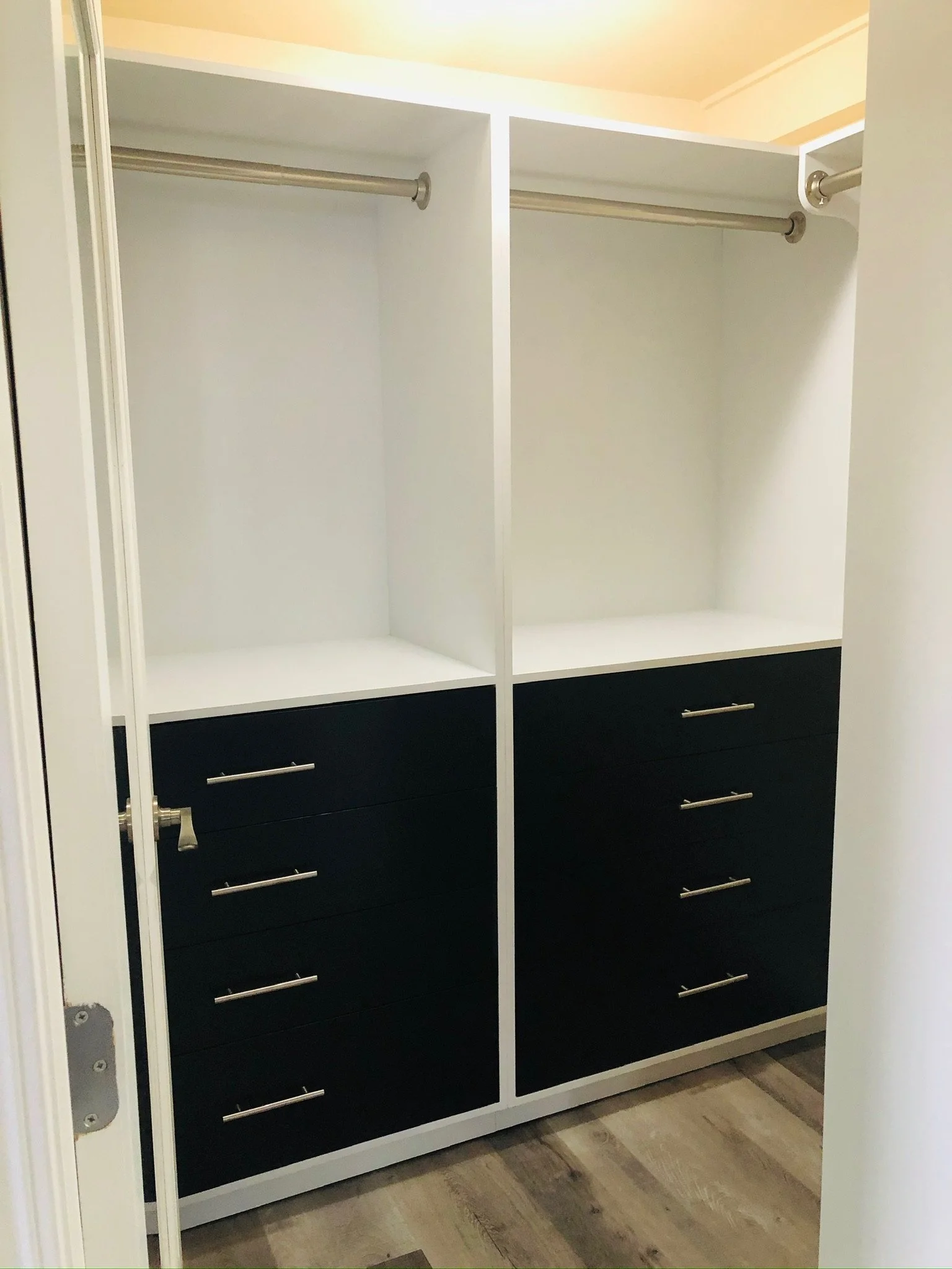 Empty closet with black drawers at the bottom, white frame, two metal rods for hanging clothes, and hardwood floors.