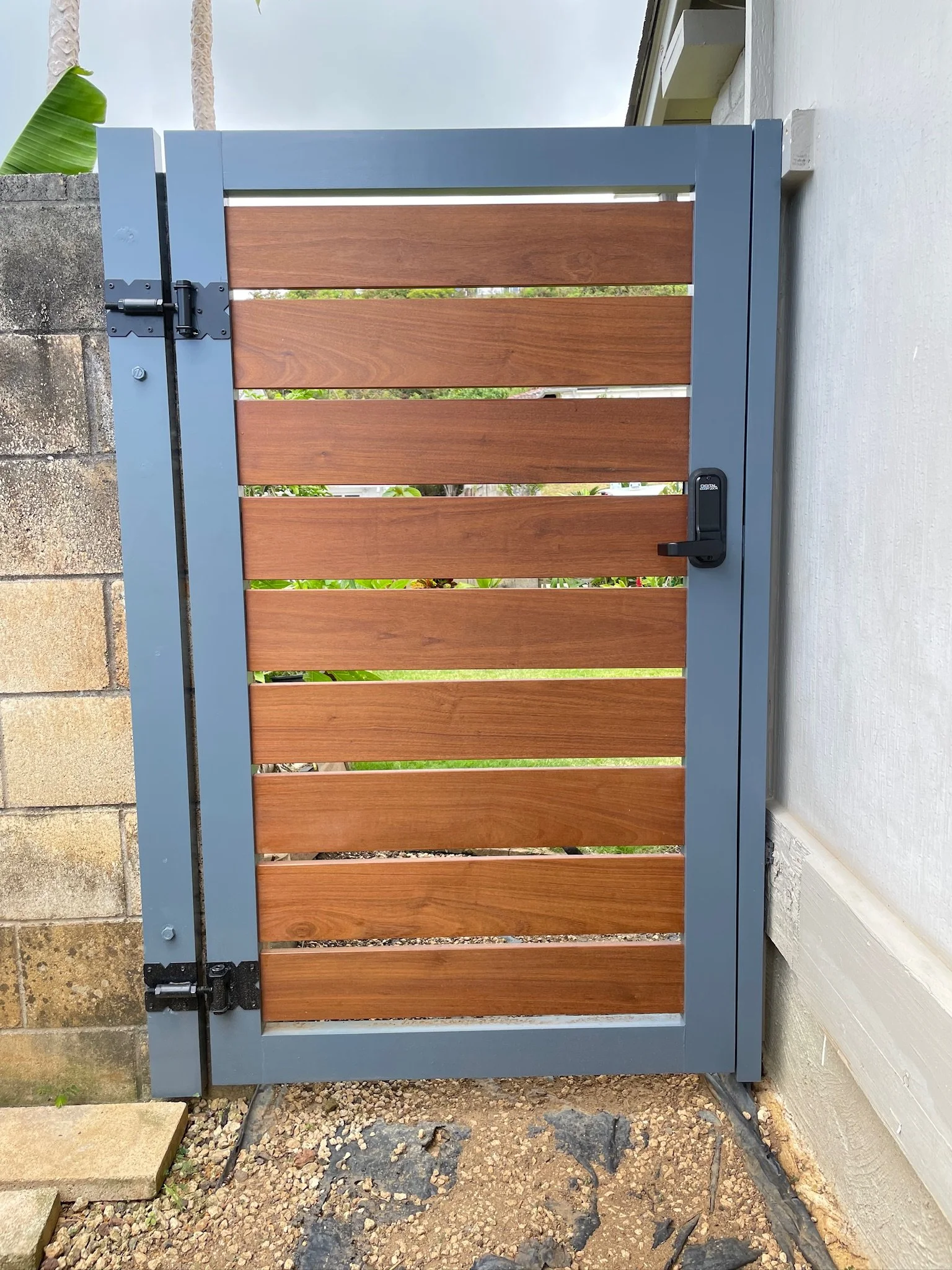 A gate with wooden slats and a gray metal frame, attached to a concrete wall on one side, with a lock and hinges visible.