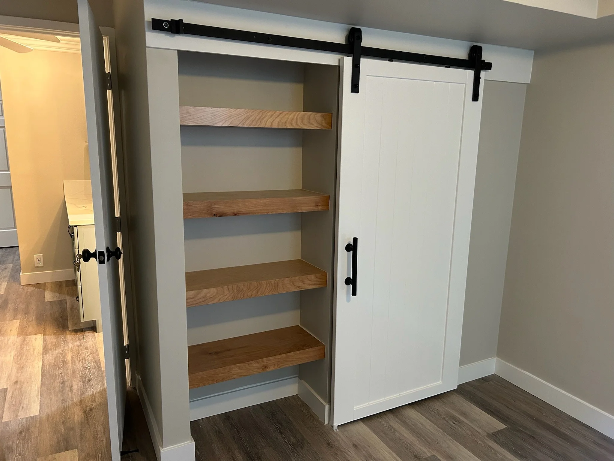 An open kitchen cabinet with black sliding barn doors revealing wooden shelves inside.