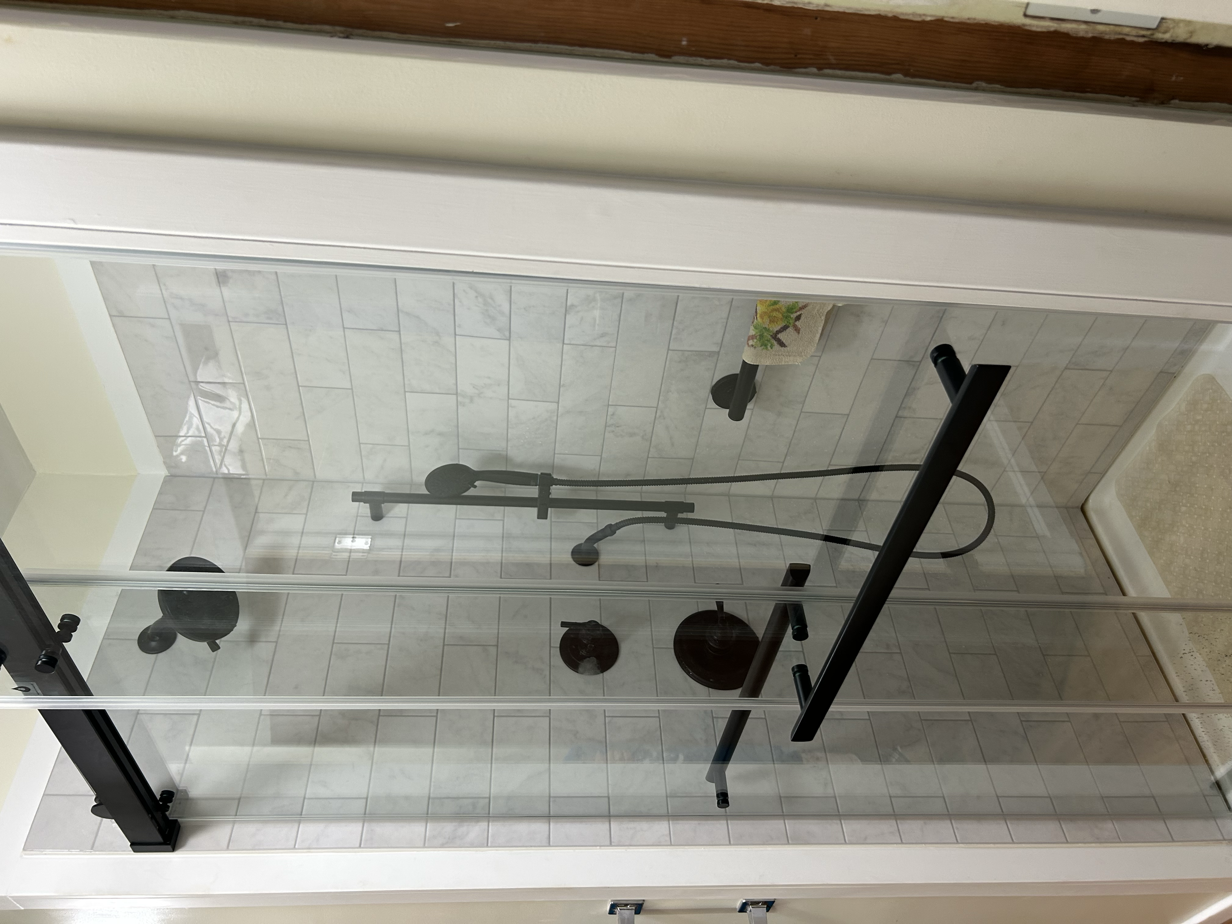 A clean, modern shower upgrade featuring marble-look tile, a glass sliding enclosure, and matte black fixtures. Complete with an overhead shower, handheld shower system, and coordinated accessories for a functional and polished finish.