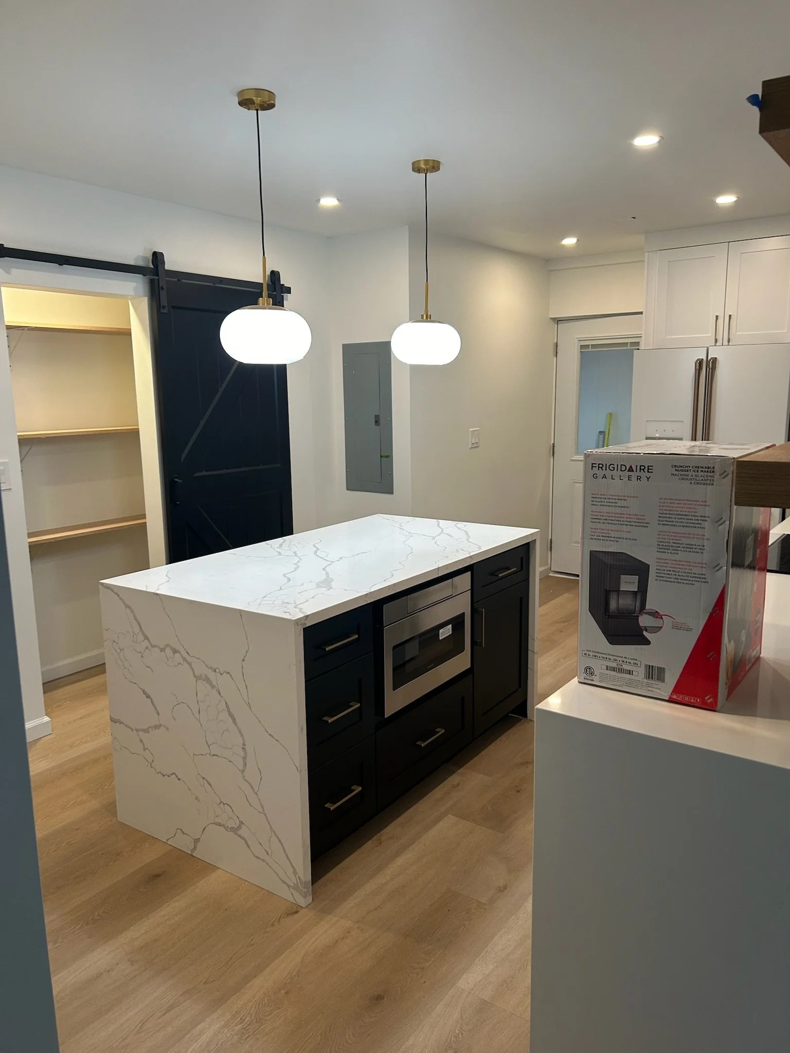 Modern kitchen with a white marble island, black cabinetry, white upper cabinets, and pendant lights, with an open pantry and new appliances.