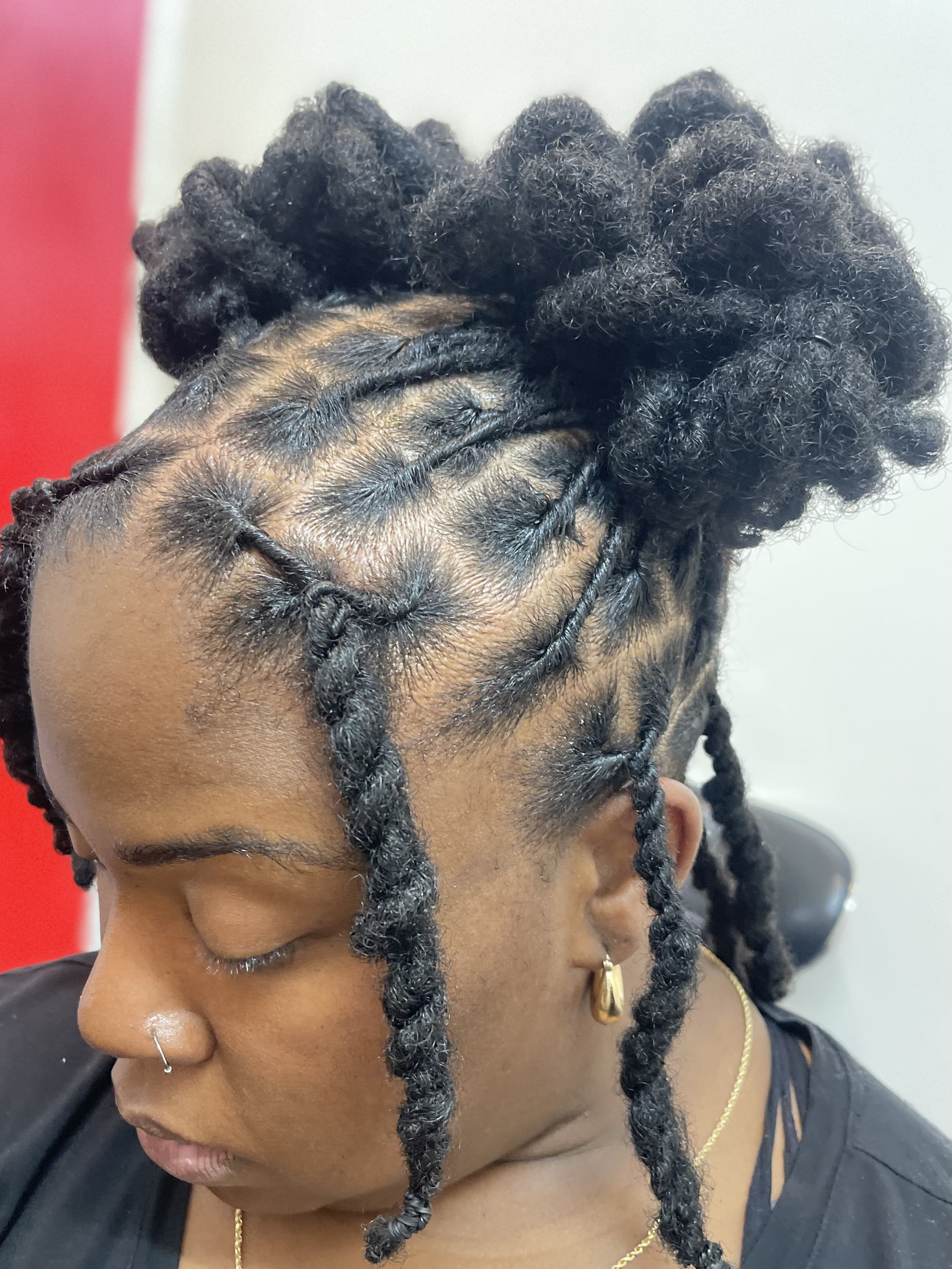 Close-up of a person with styled black dreadlocks and gold jewelry, with a red and white background.