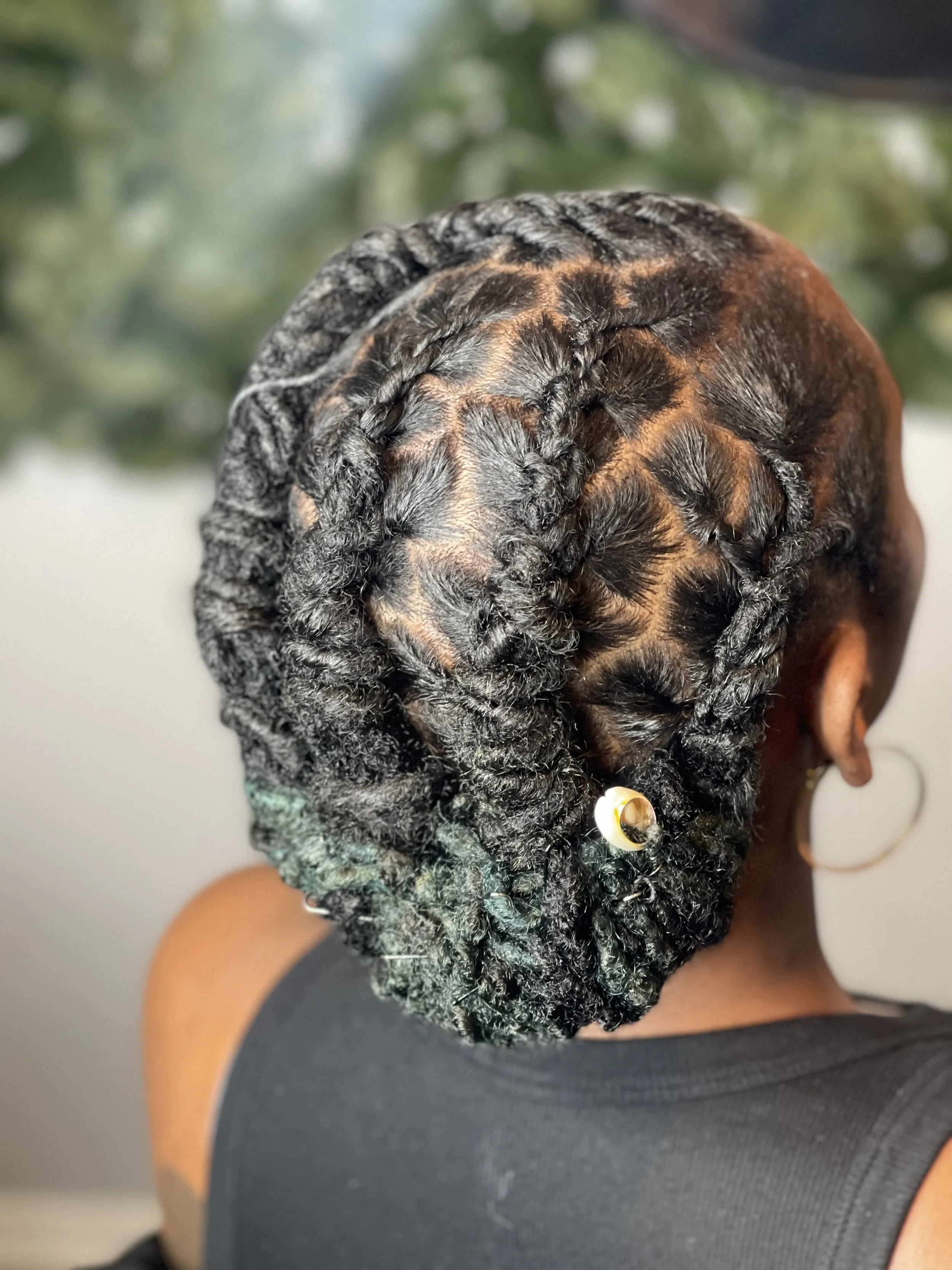 A person with braided hair and curly extensions, wearing a earring and a sleeveless black top.