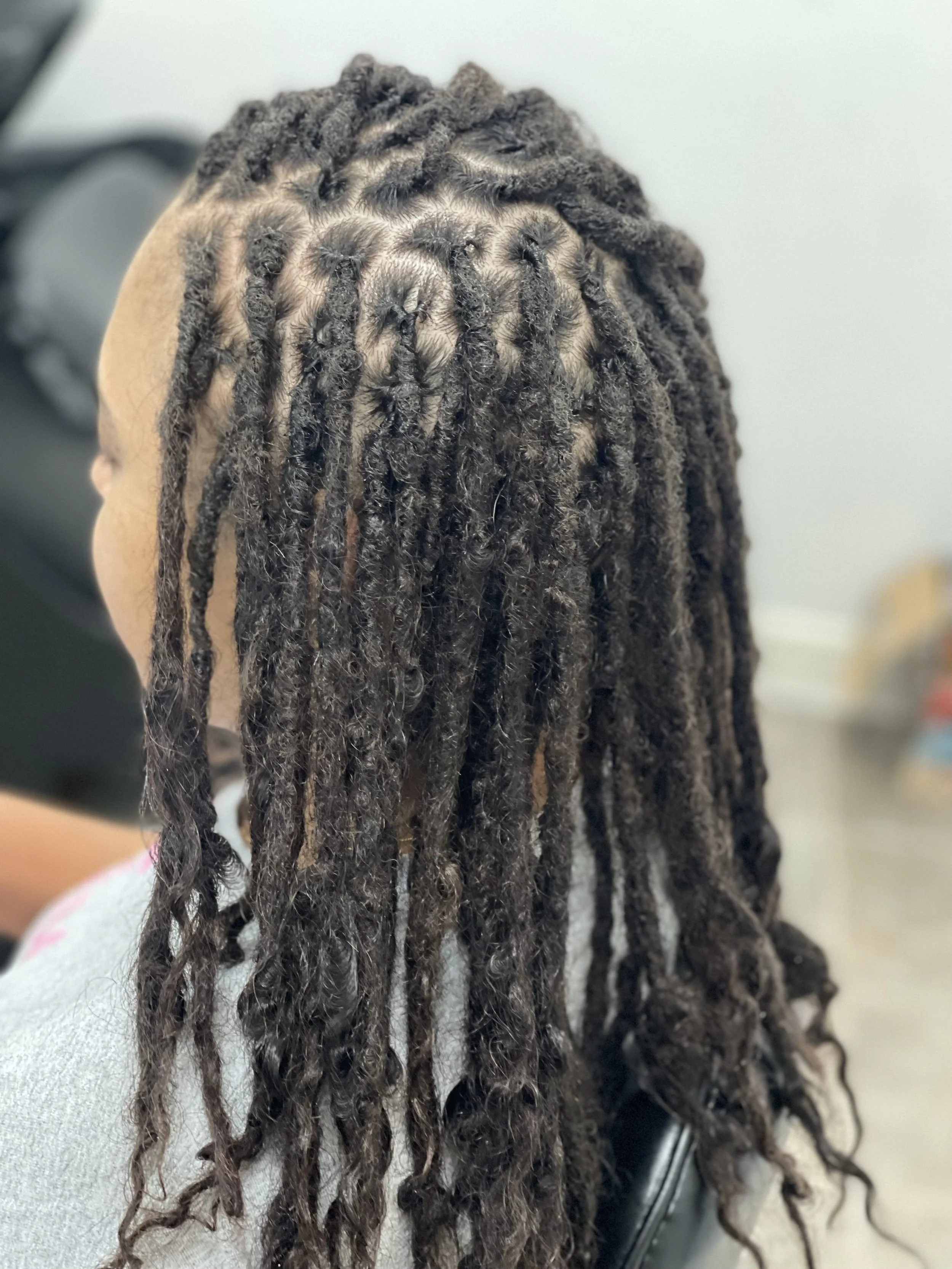 Close-up of dark brown dreadlocks with some lighter strands, hanging over a person's shoulder, against a neutral background.