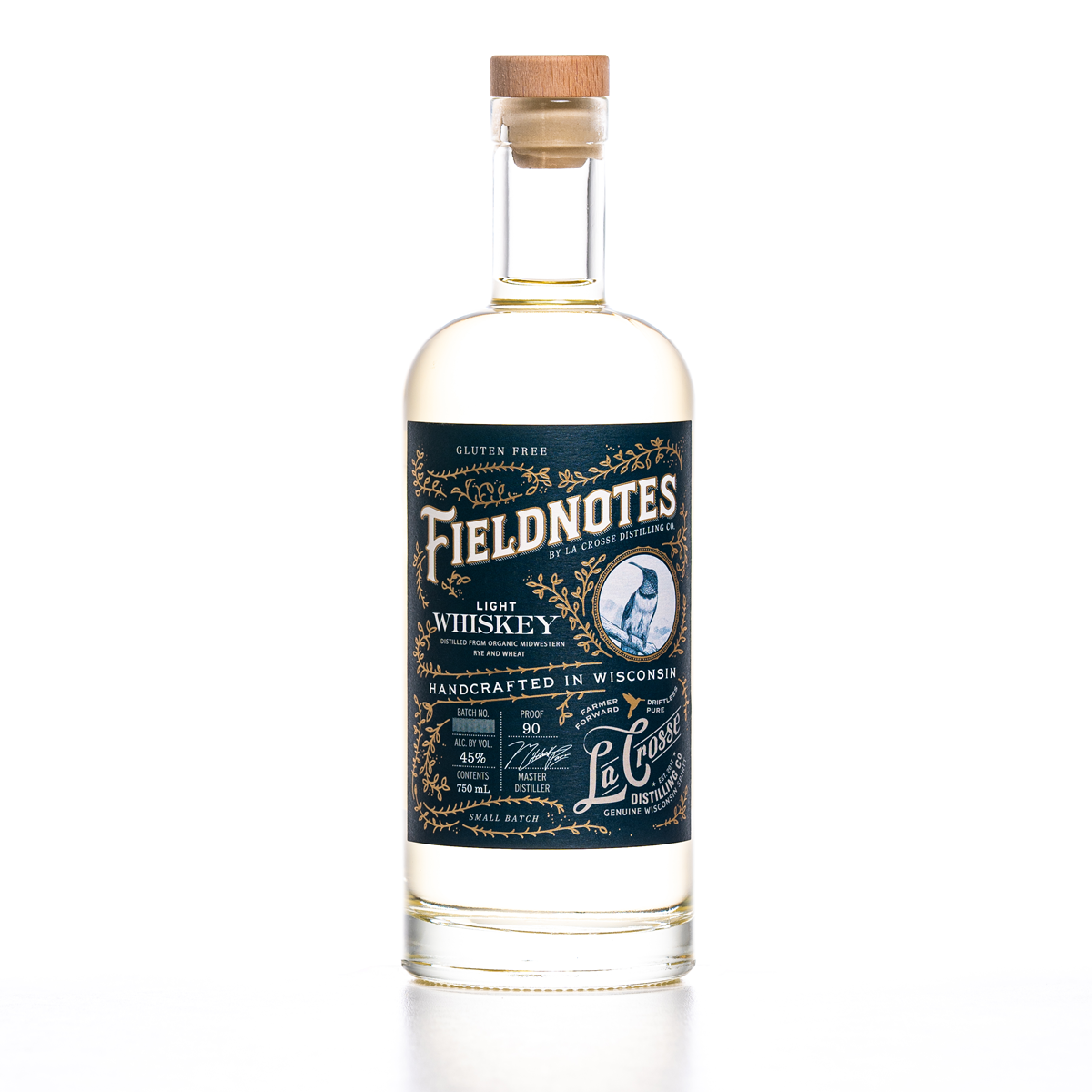 A clear glass bottle of Fieldnotes Light Whiskey with a black and gold label, wooden cap, and white background.