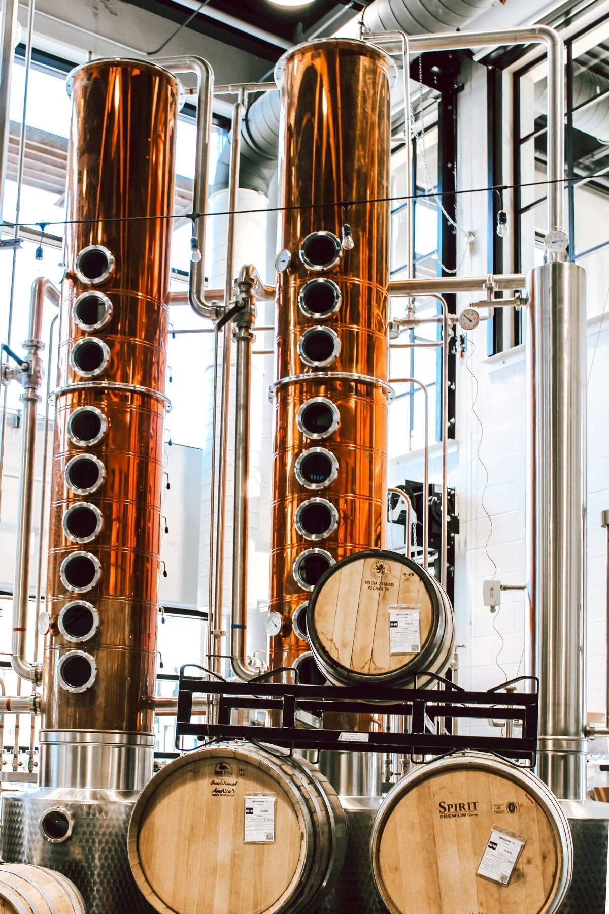 Copper distillation columns and wooden barrels inside a distillery.