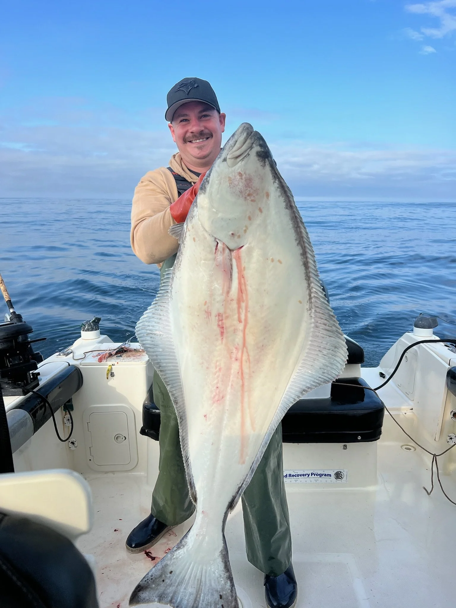 A man smiling on a boat holding a large halibut fish