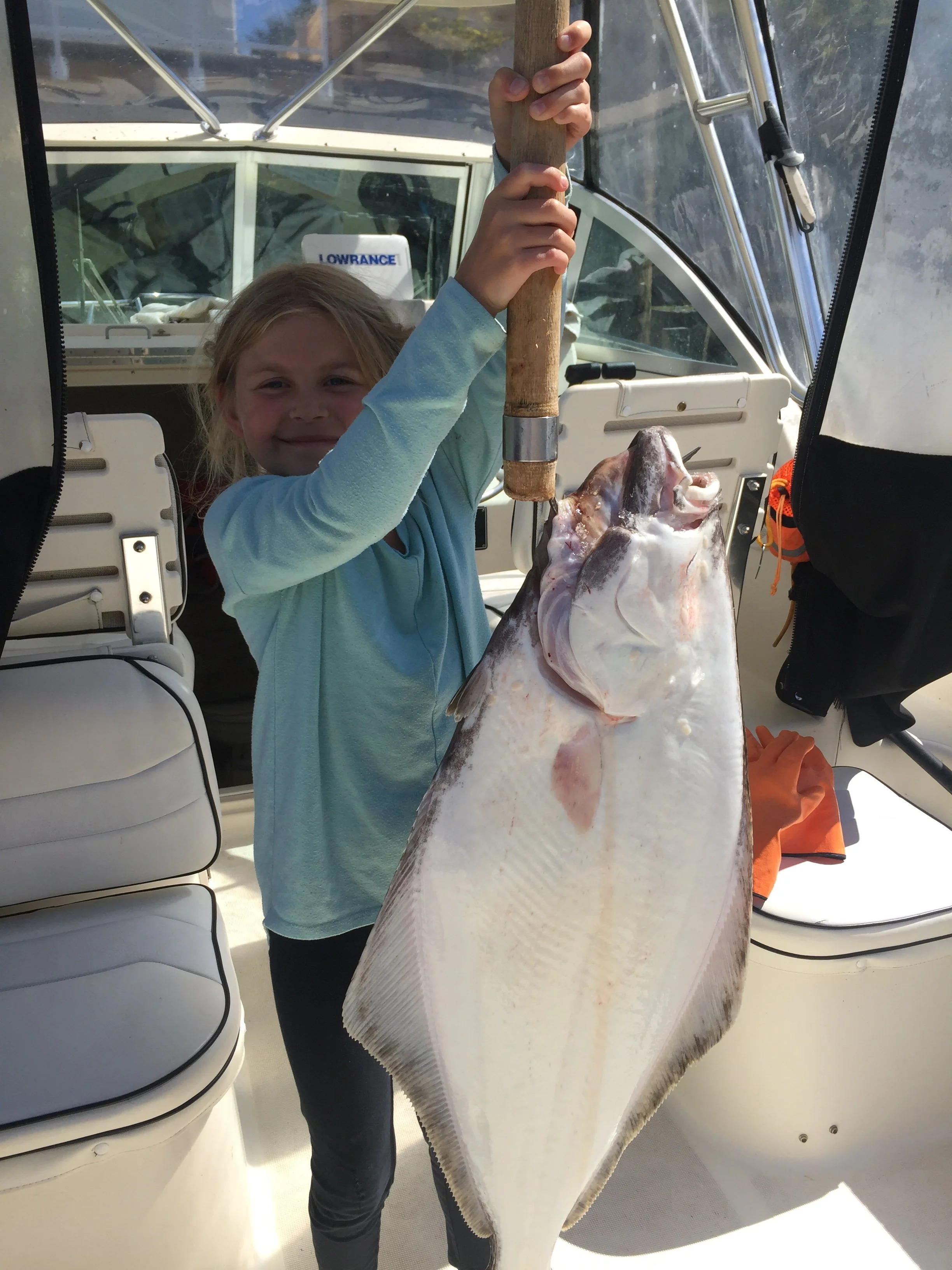 A young girl on a boat holding a large fish by the gills.