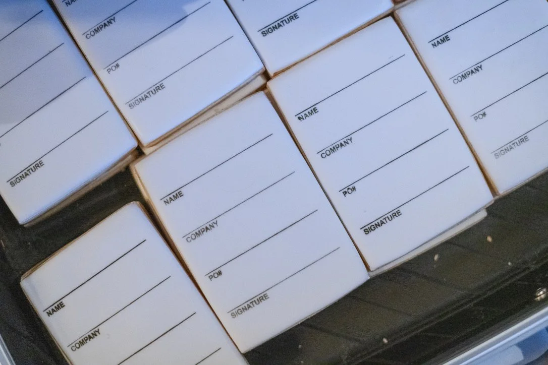 Multiple blocks of paper forms labeled for name, company, P.O. number, and signature, stacked in a box.