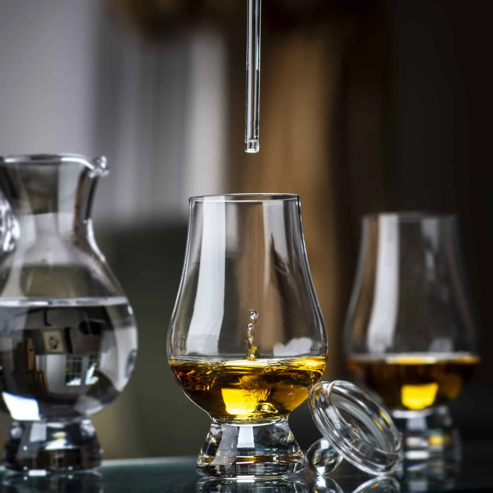 A glass pipette carefully dropping water into a glass of whiskey