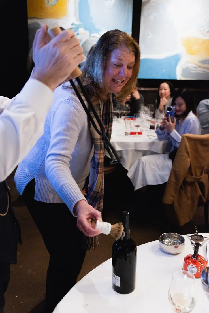 A volunteer from the audience assists in Port tonging by applying a freezing cold shave brush to the hot neck of the bottle, causing thermal shock that allows the bottle to be open below the cork.
