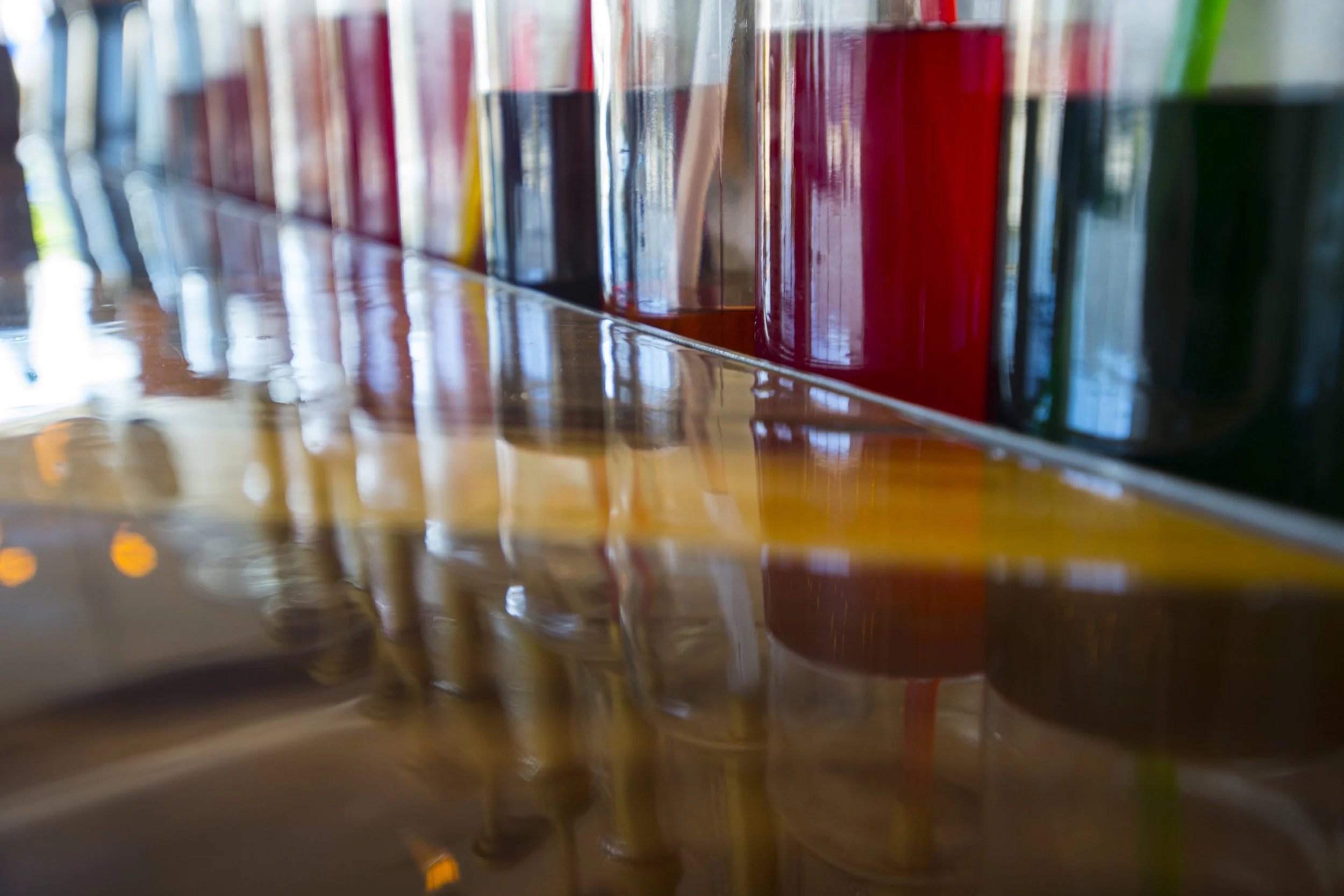Close-up of colorful sauce bottles on a bar with reflections on a polished wooden surface.