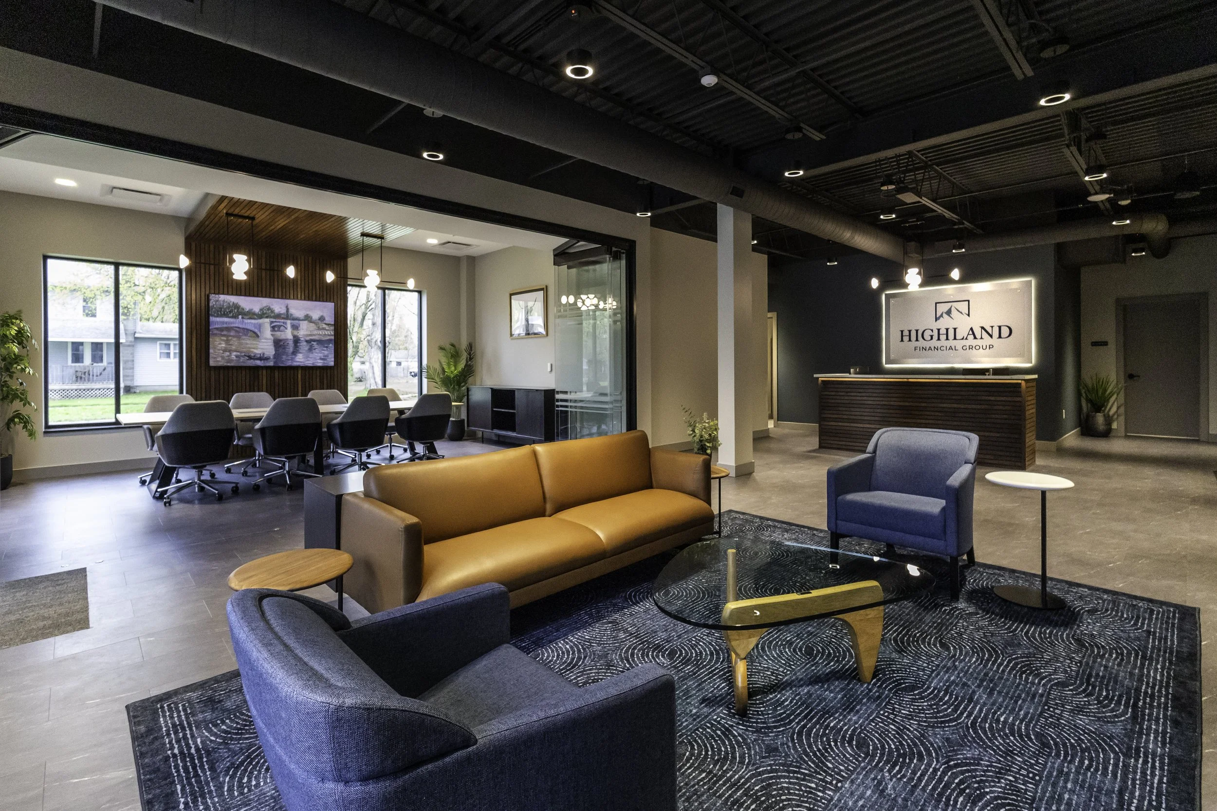 Modern office reception area with lounge seating, a conference room with chairs and a large screen, and Highland Financial Group signage illuminated on the wall. Large windows let in natural light, and plants add to the decor. Interior Design.