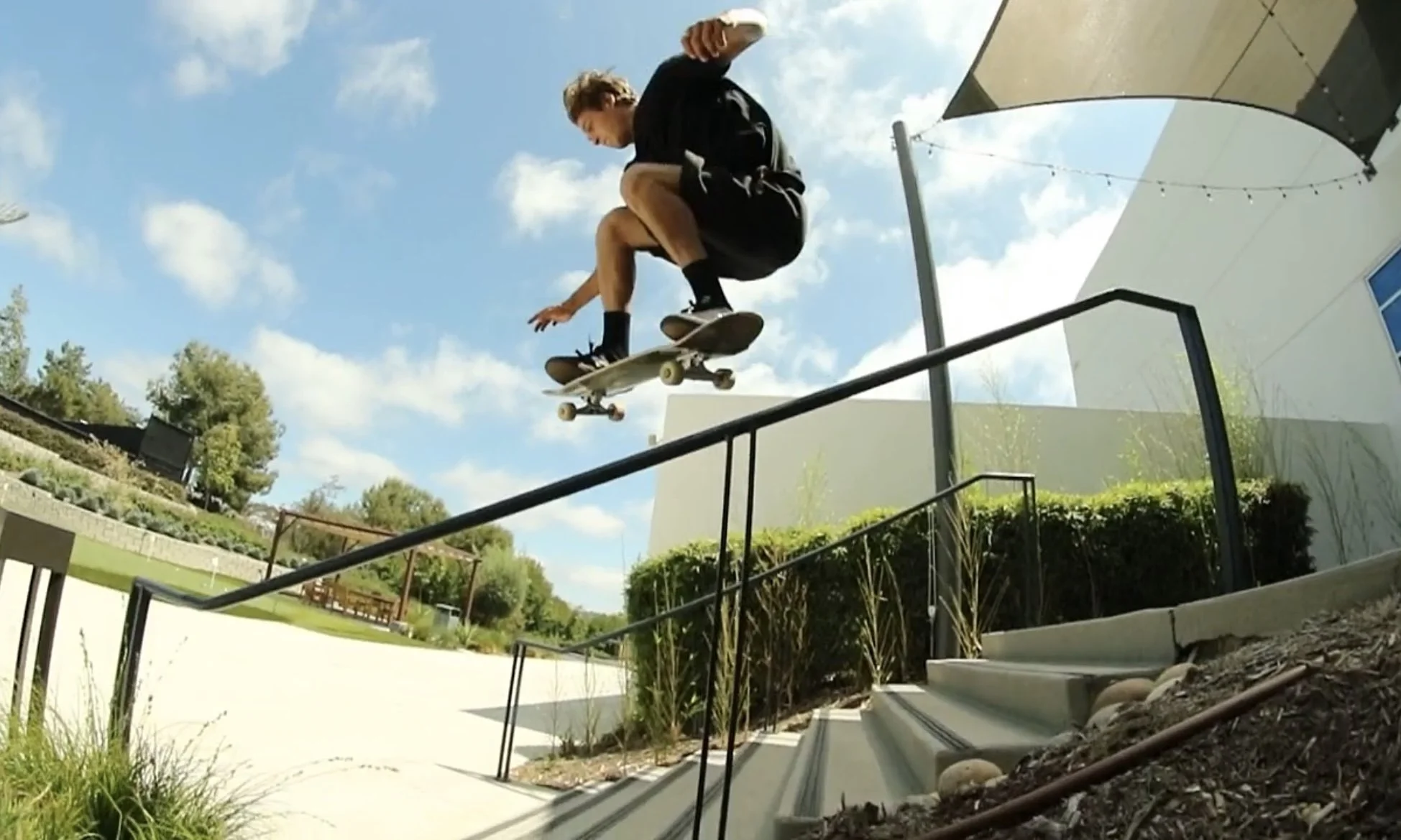 A skateboarder performing a trick on a handrail outdoors under a partly cloudy sky.
