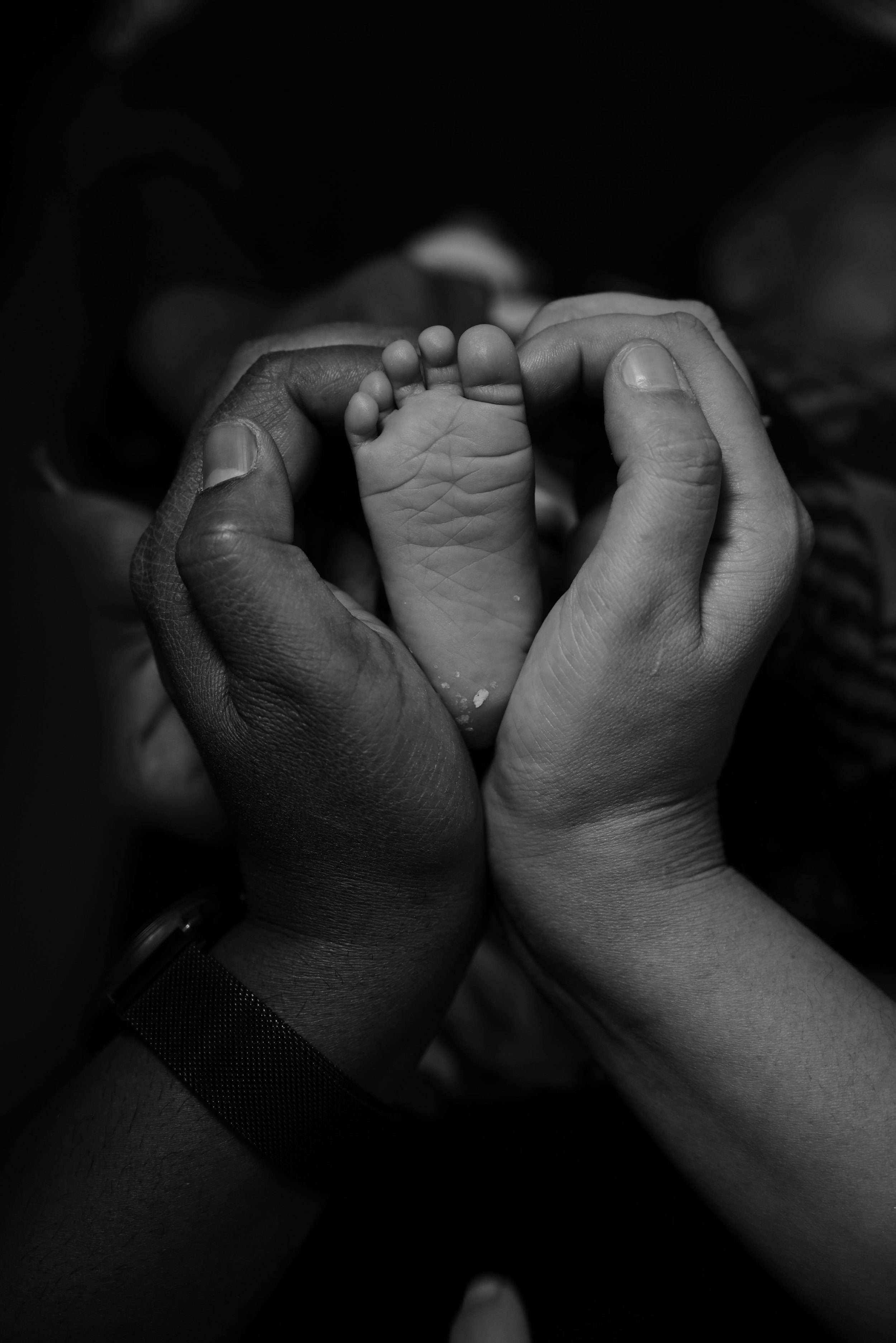 A close-up photograph showing adult hands holding a tiny baby's foot in black and white.