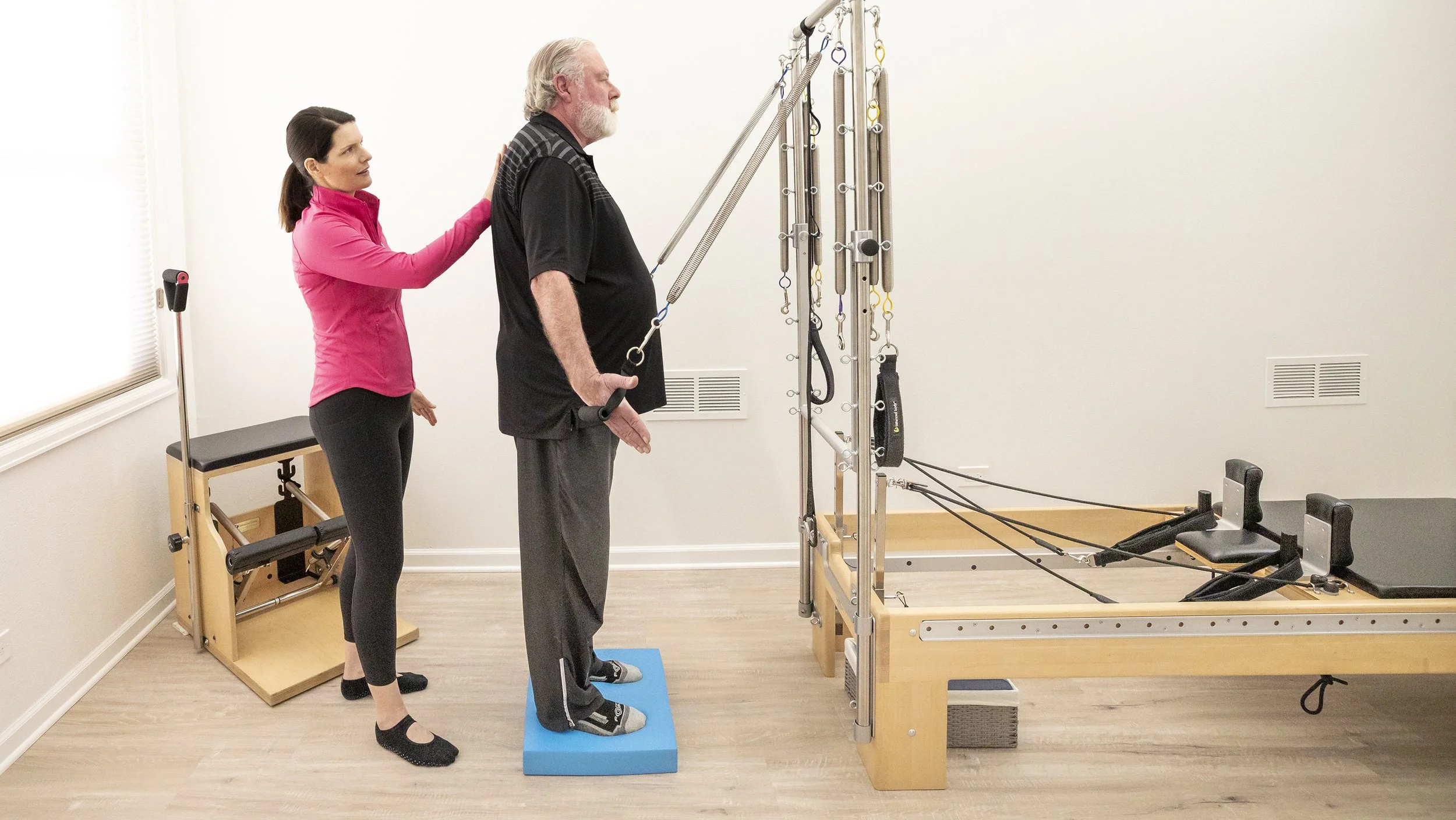 A Taylor Pilates & Fitness movement practitioner working with a senior client to build strength and balance during a private pilates session on the Pilates Reformer.