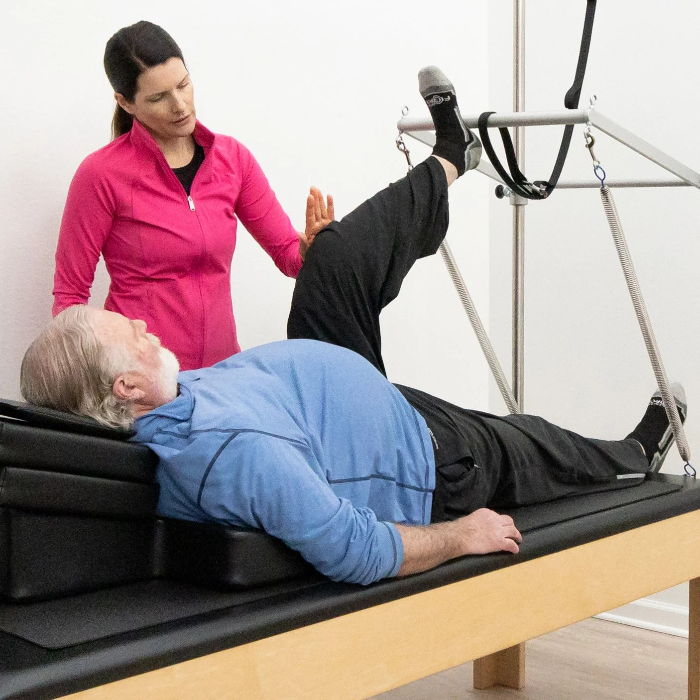 A Taylor Pilates & Fitness movement practitioner showing a senior client how to improve mobility and strength on the pilates trapeze table during a private session.