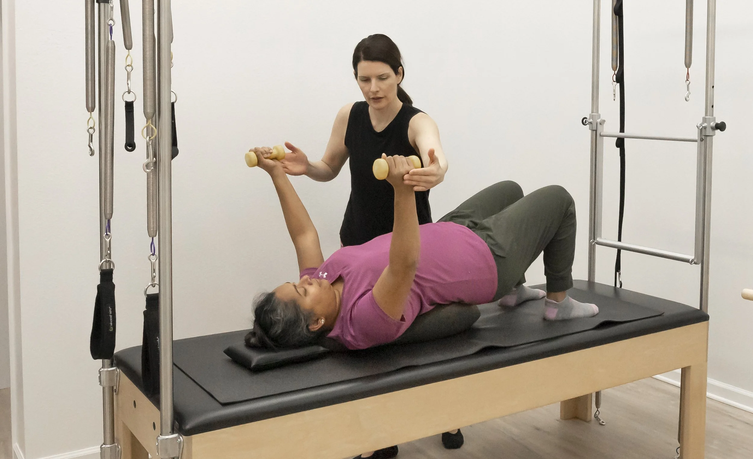 A Taylor Pilates & Fitness movement practitioner working with a client for rehabbing an injury on the trapeze table during a private pilates session.