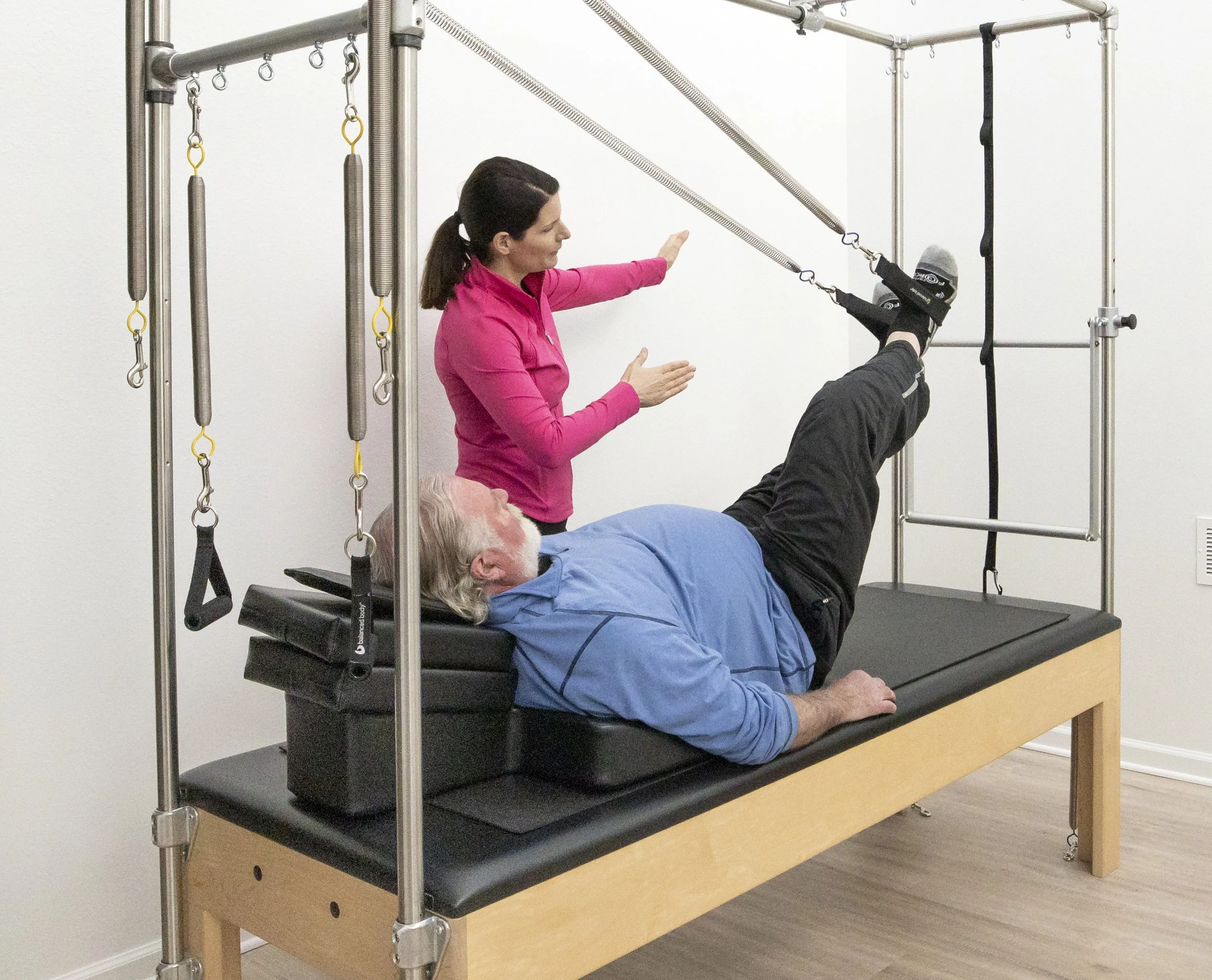A Taylor Pilates & Fitness movement practitioner working with a senior client to build strength and balance during a private pilates session on the Pilates trapeze table.