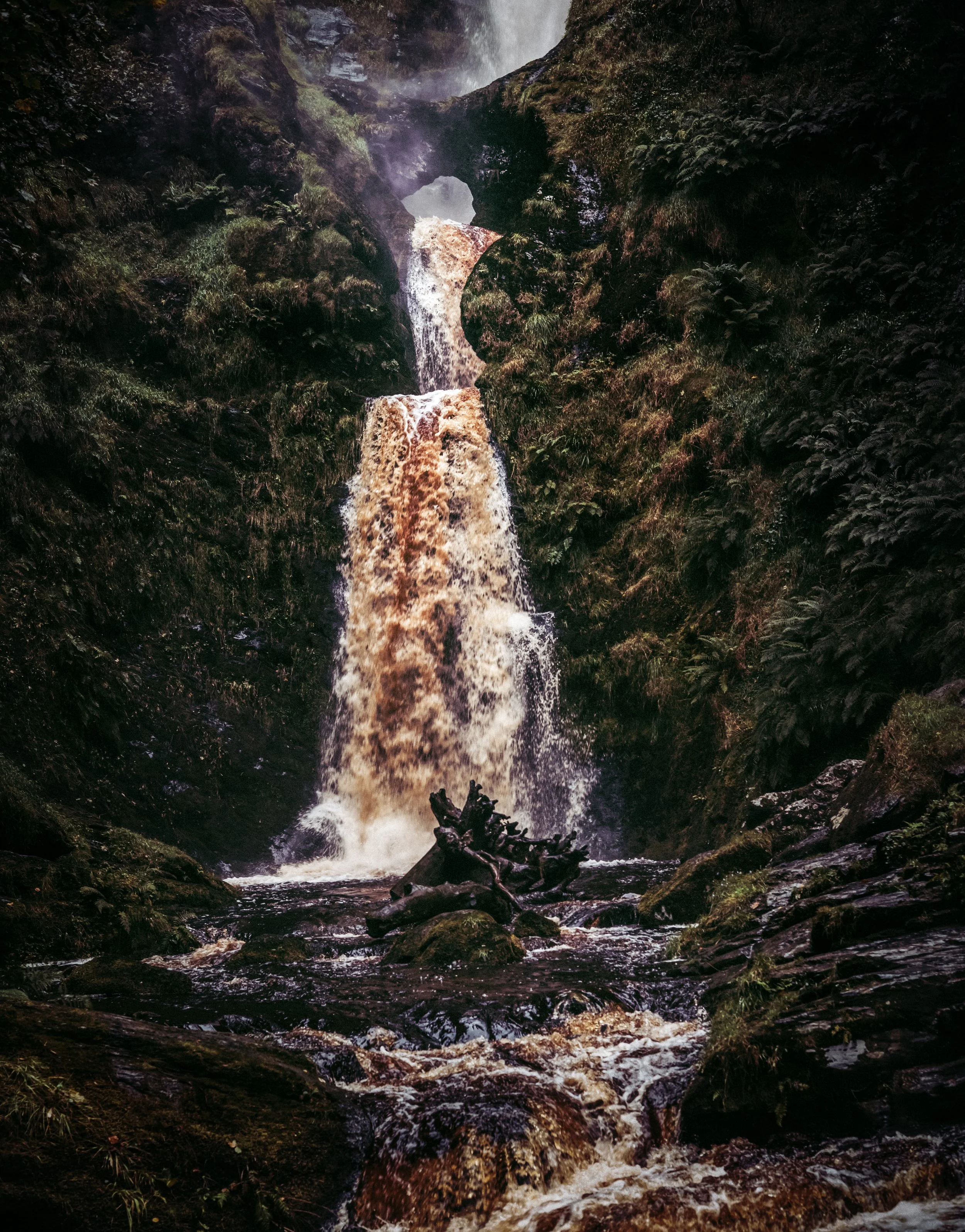 A multi-tiered waterfall flowing through a rocky, moss-covered landscape in a forest.