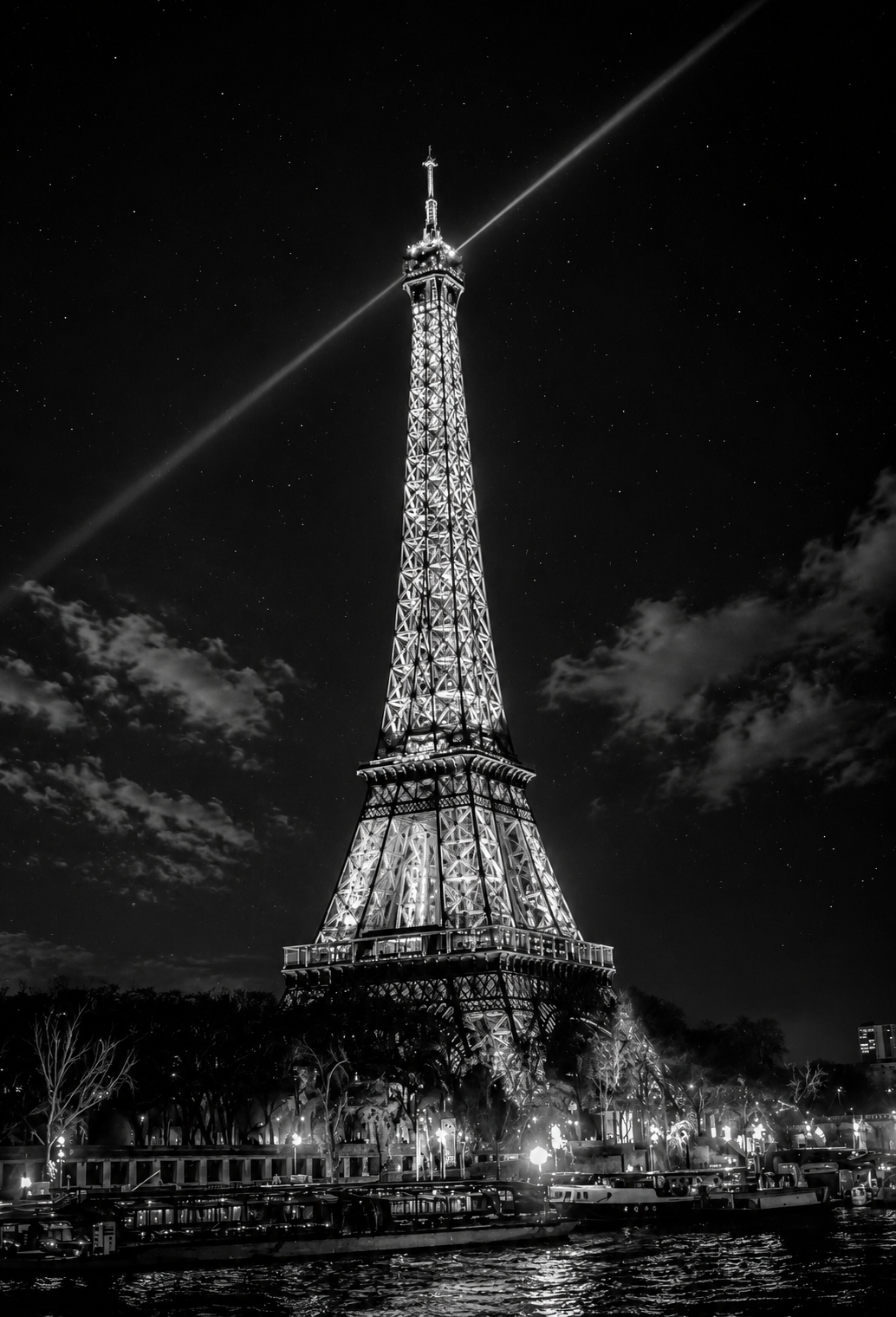 Nighttime view of the Eiffel Tower illuminated with lights, with a starry sky and clouds in the background.