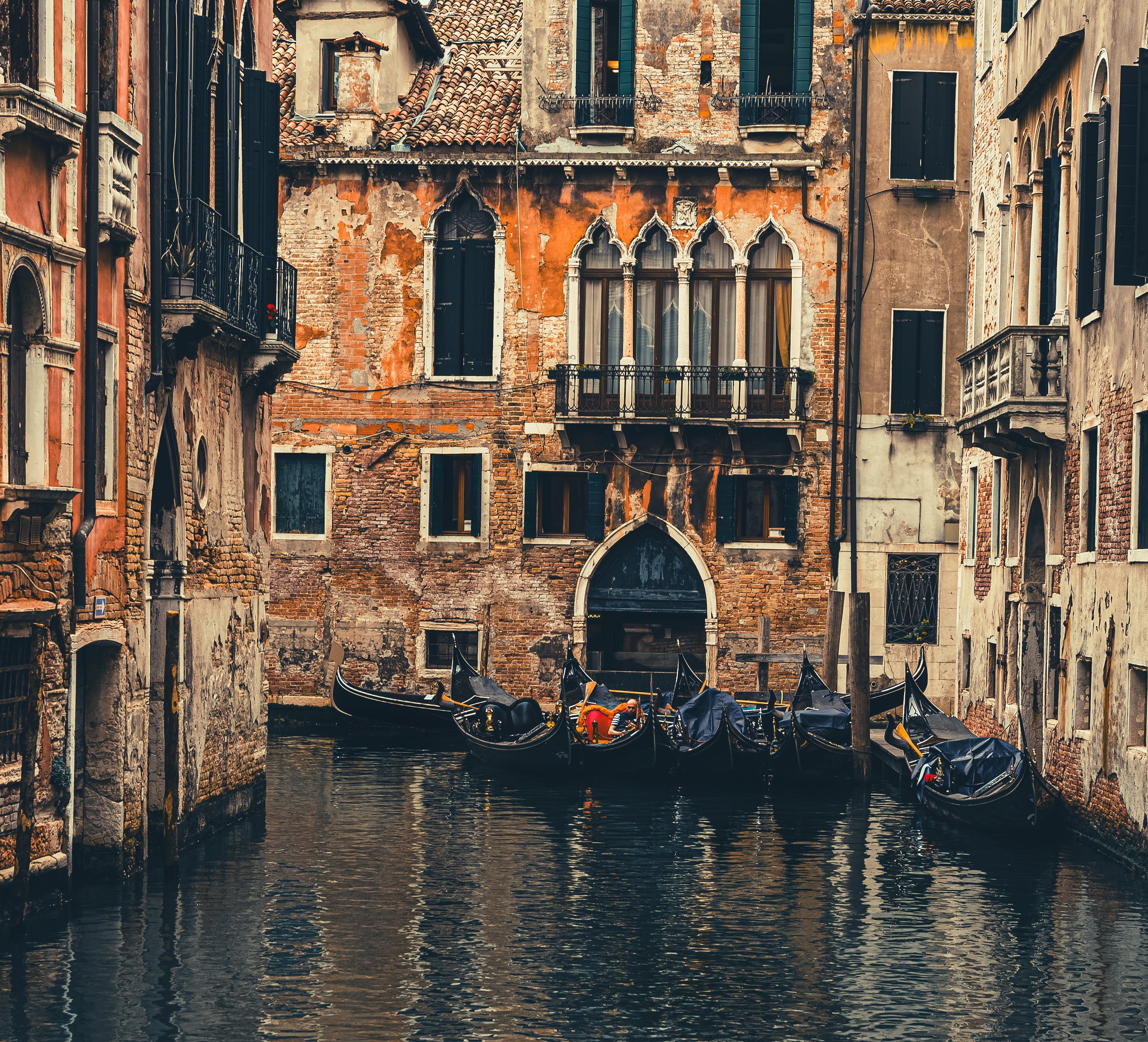 Gondolas floating on a canal amid historic, weathered buildings in Venice, Italy.