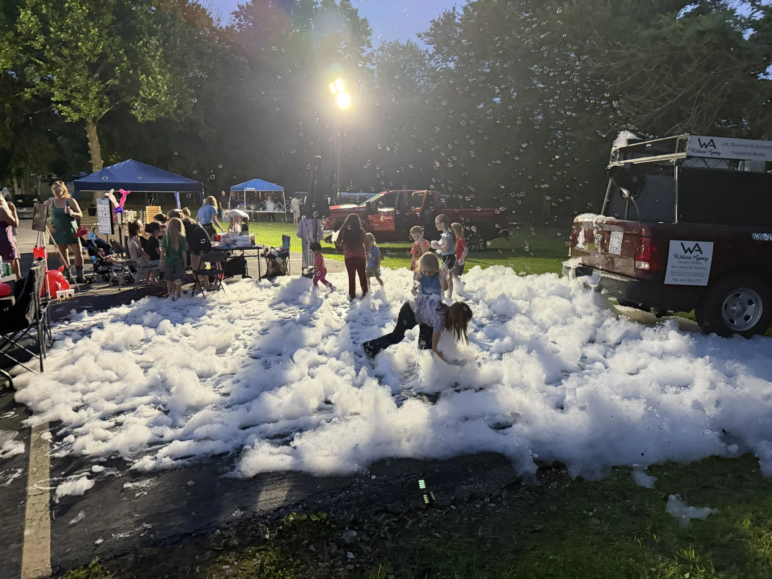 End of the community event, foam party is dissipating and the sun is setting , we see various tents of other vendors in background