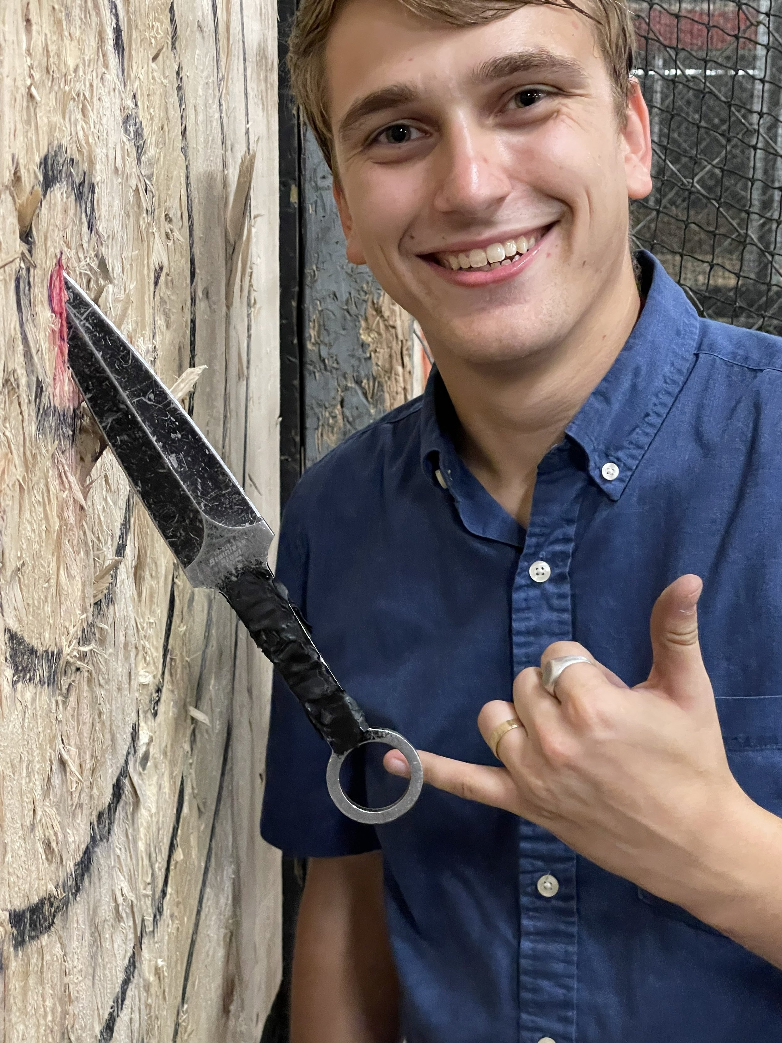 A smiling young man with light brown hair giving a shaka with left hand, standing next to a blade that made a perfect bullseye